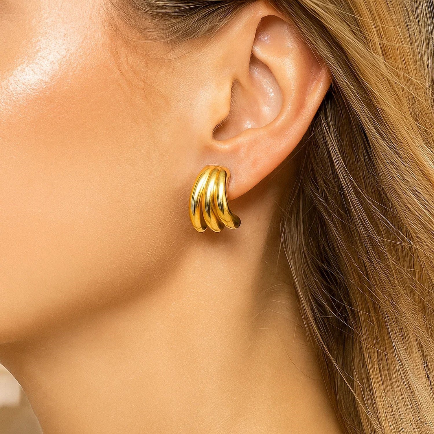 A woman wears a 14K yellow gold triple row splayed hoop earring.