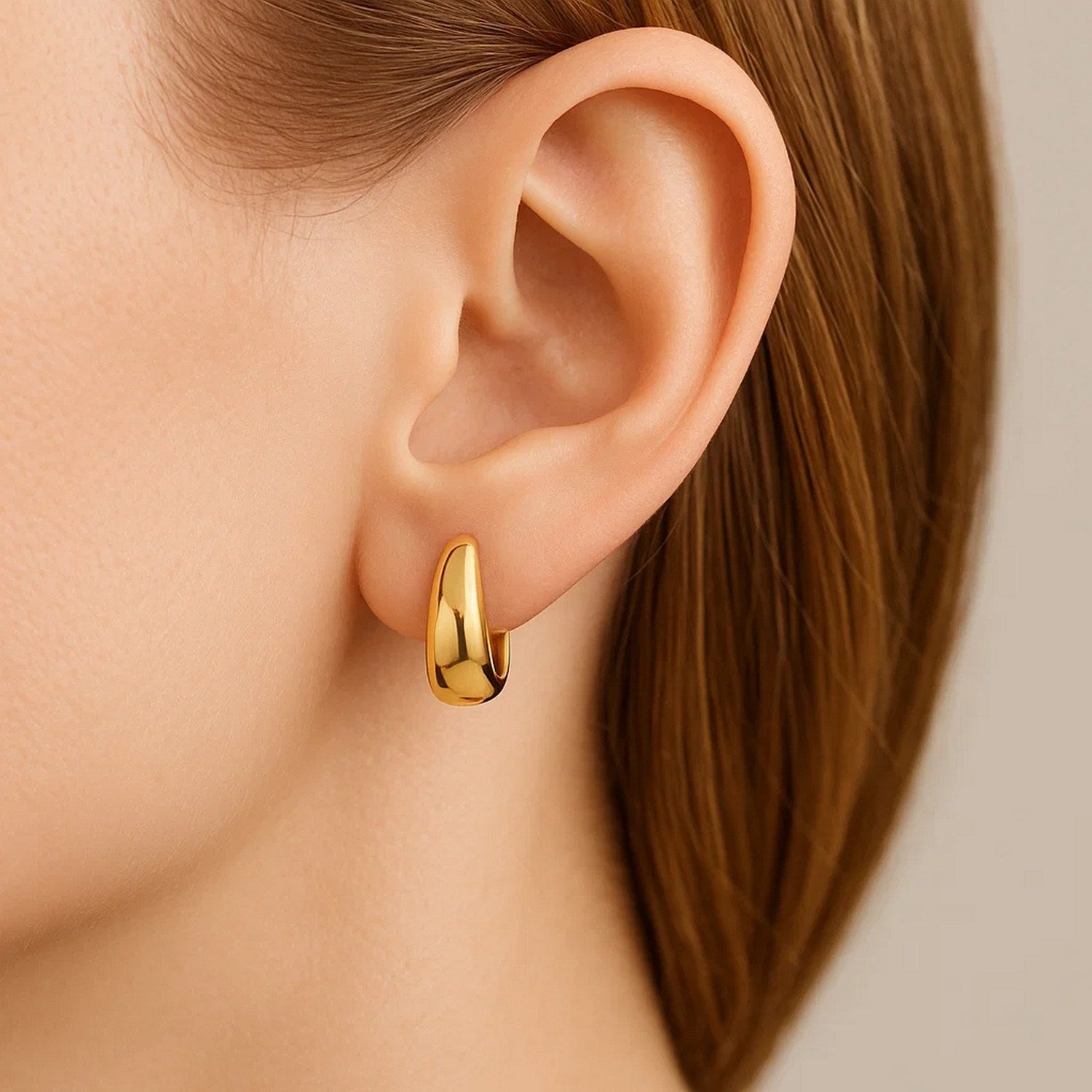 Tapered 14K yellow gold huggie hoop earring on a person's ear.