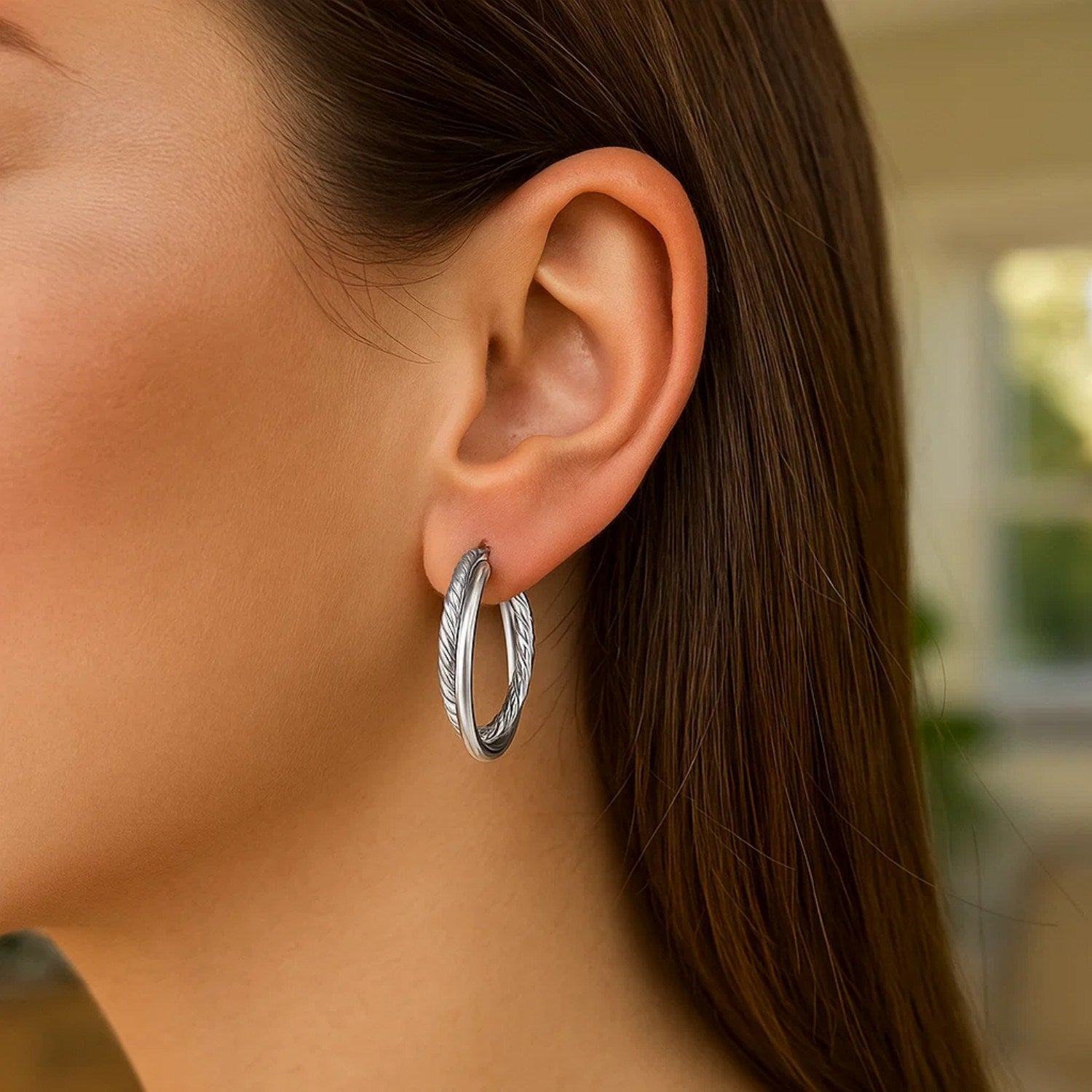 Sterling silver ridged hoop earrings with a textured design are worn on a woman's ear.