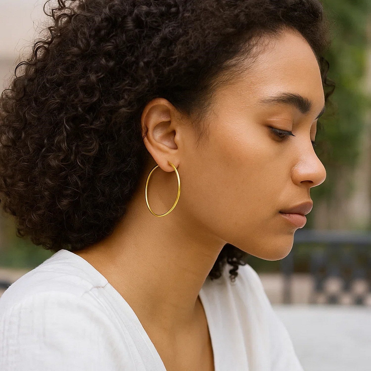 Endless hoop style earrings in 14K yellow gold on a woman with curly hair.