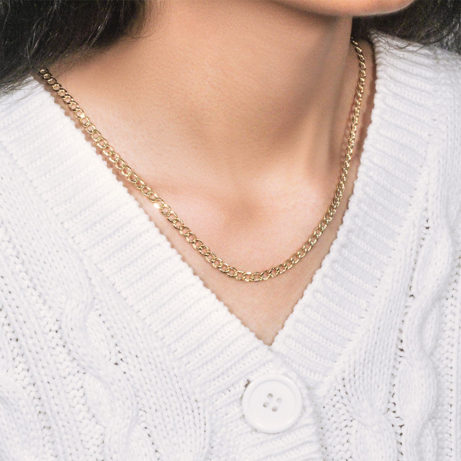 A 10k yellow gold curb chain is worn around a person's neck over a white sweater.