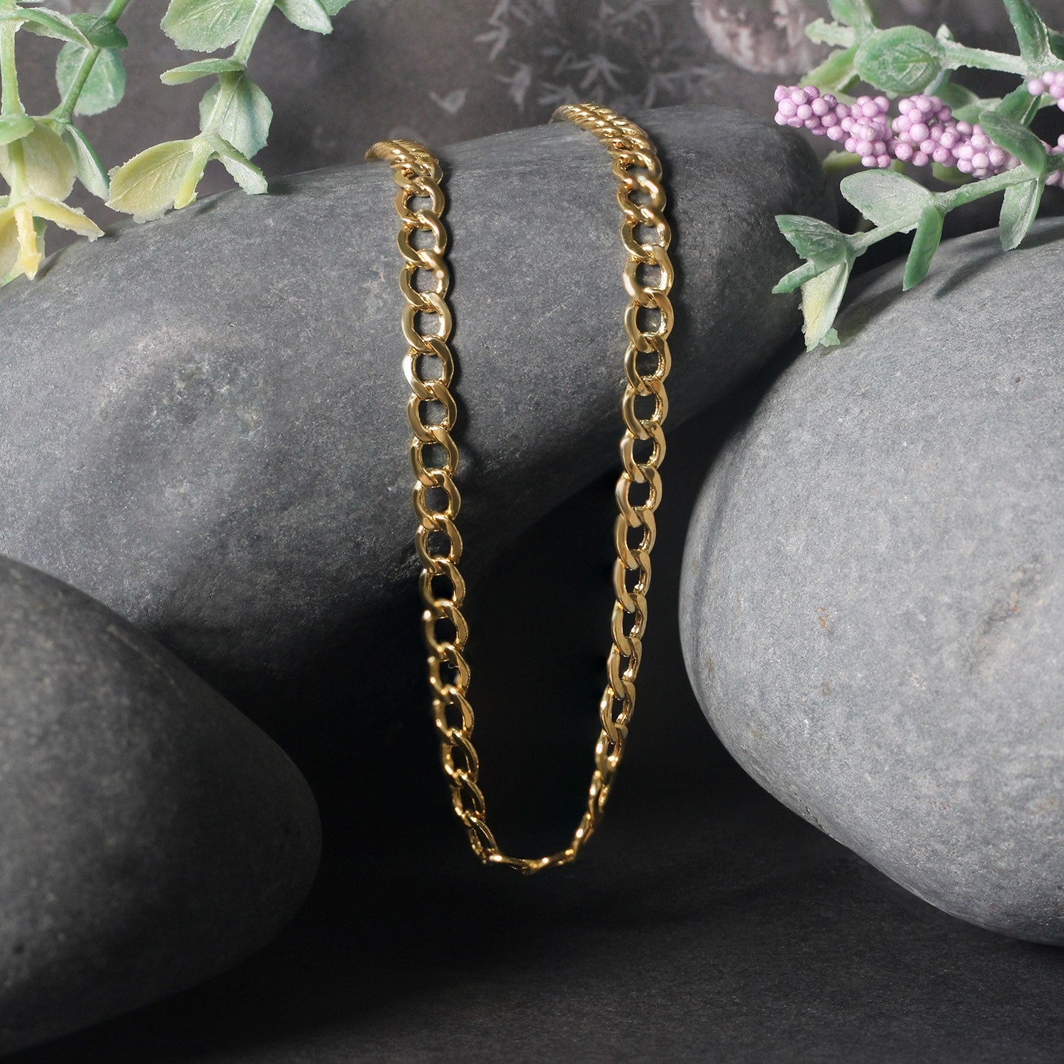 A 10k yellow gold curb chain is draped over gray stones with floral accents.