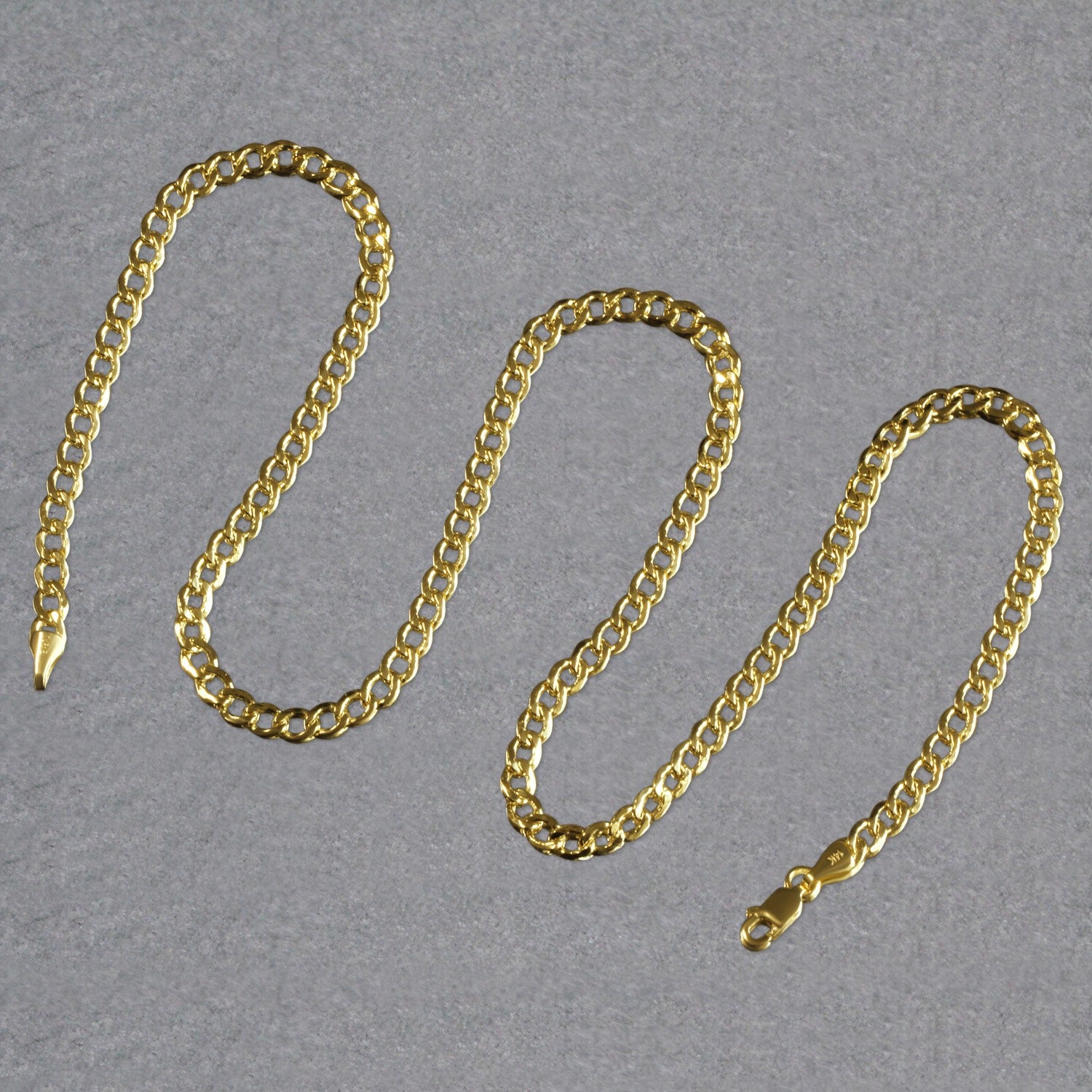 A 10k yellow gold curb chain with a lobster clasp is arranged in a wavy pattern.