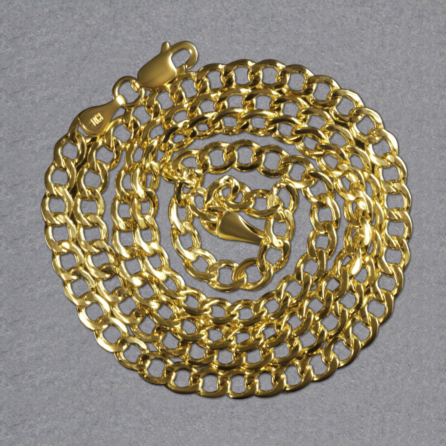 A 10k yellow gold curb chain with a lobster clasp, coiled on a gray surface.