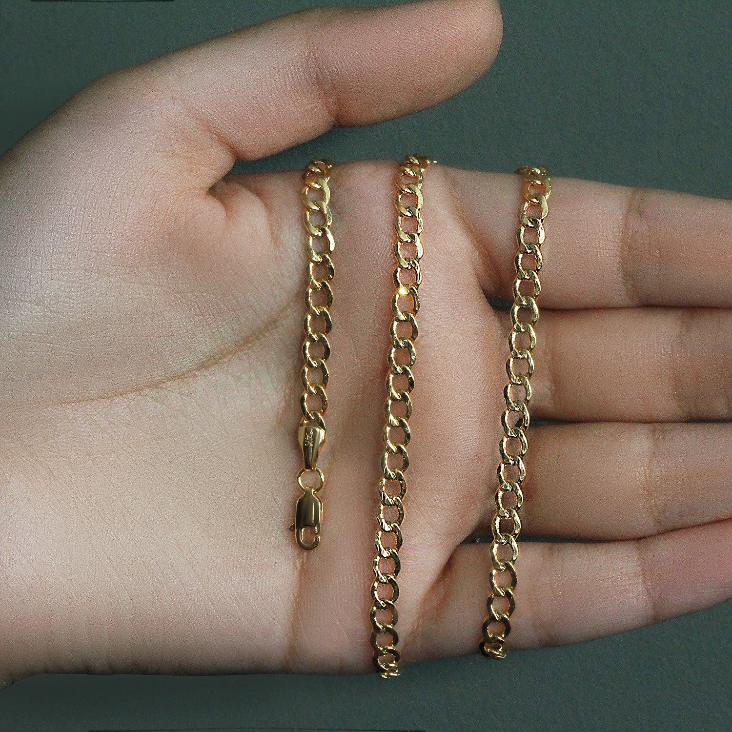 A 10k yellow gold curb chain with a lobster clasp is displayed on a hand.
