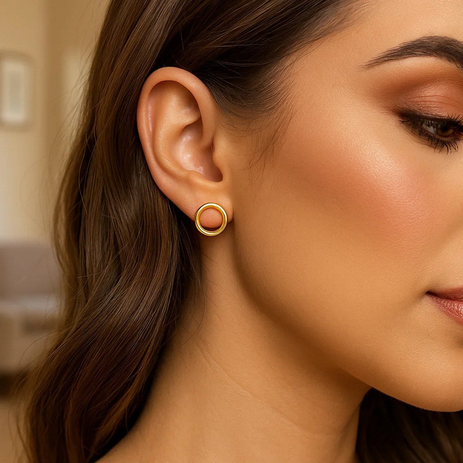 A woman wears a single shiny open circle post earring in 14k yellow gold.