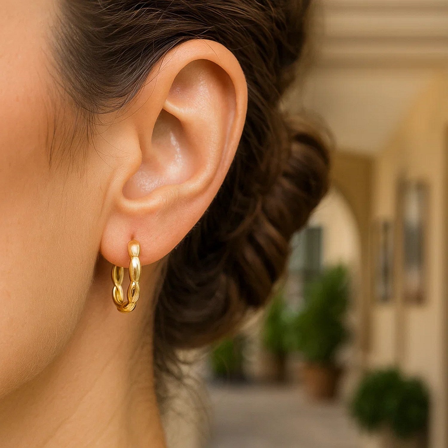 Medium 14K yellow gold rice hoop earring on a woman's ear.
