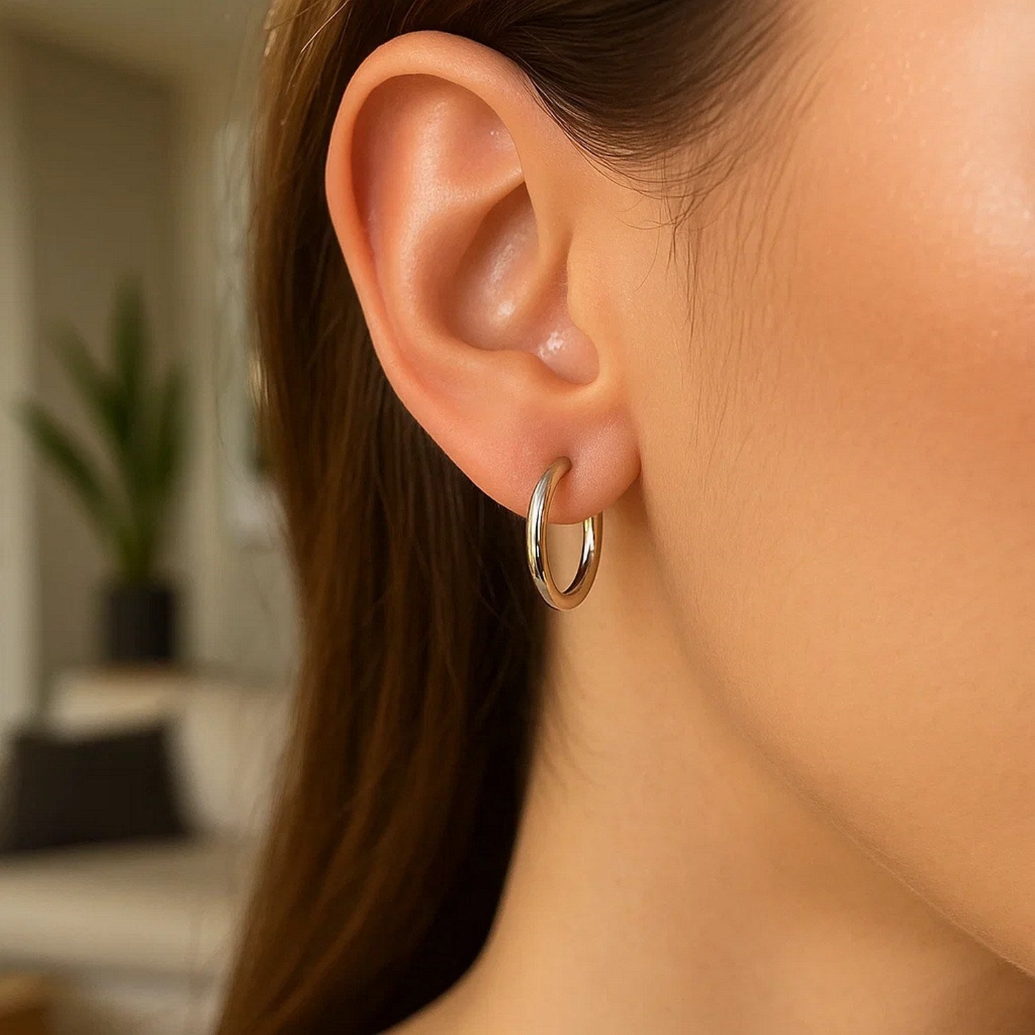 A woman wears a single polished sterling silver and rhodium plated hoop earring.