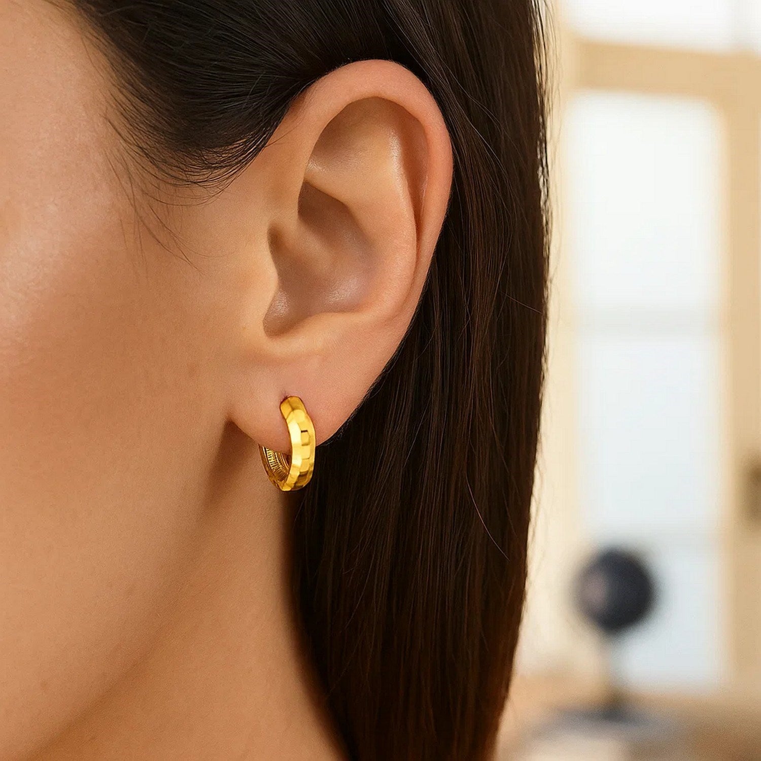 14K yellow gold checkerboard huggie hoop earring on a person's ear.