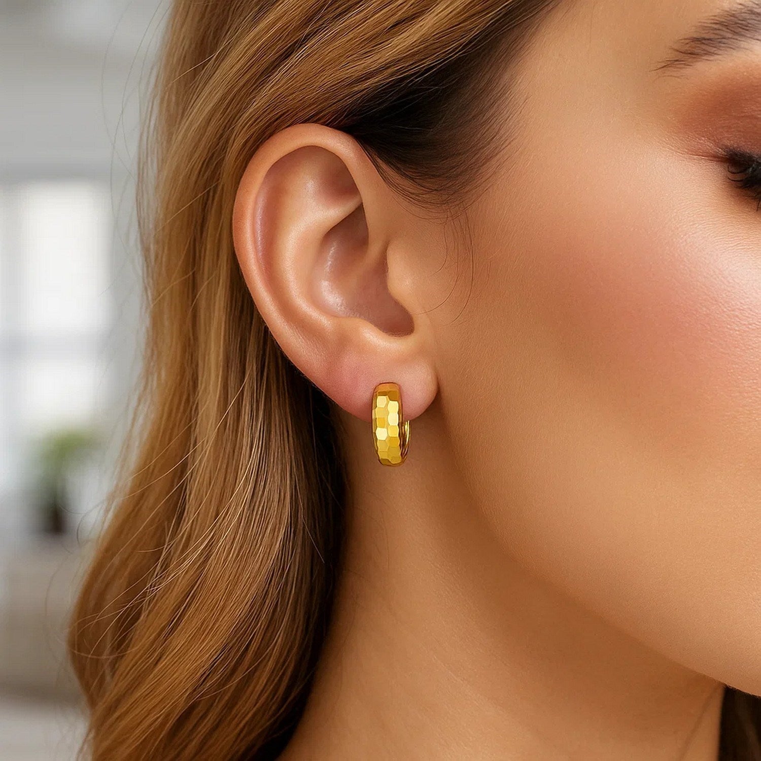 A woman wears a single 14K yellow gold checkerboard huggie hoop earring.