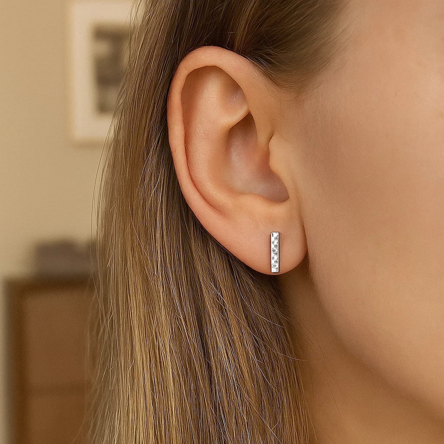 A woman wears a single 14k white gold textured bar earring on her earlobe.