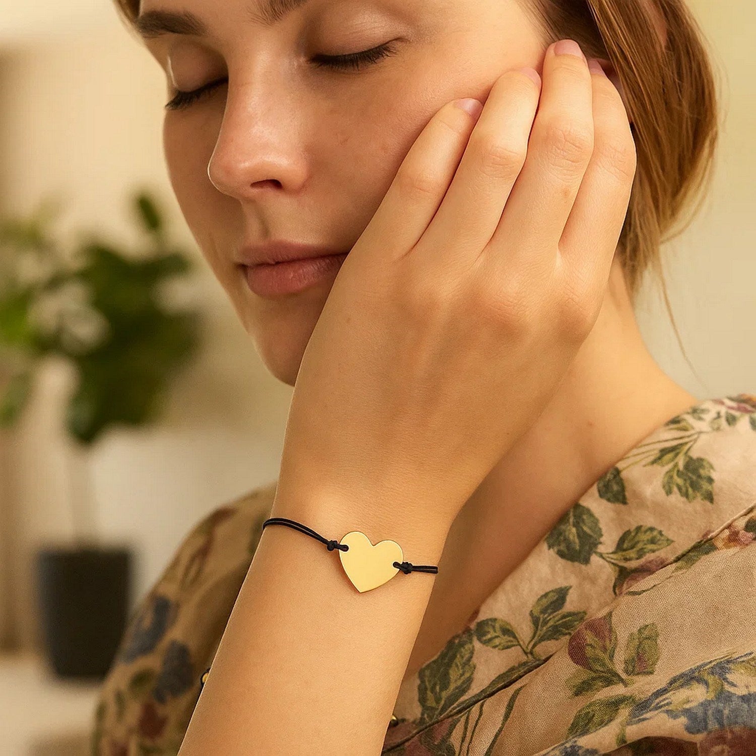 Adjustable black cord bracelet with a 14k yellow gold heart charm on a woman's wrist.