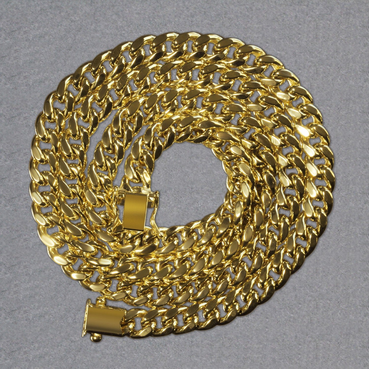 14k yellow gold semi-solid Miami Cuban chain with a box clasp, coiled on a gray surface.