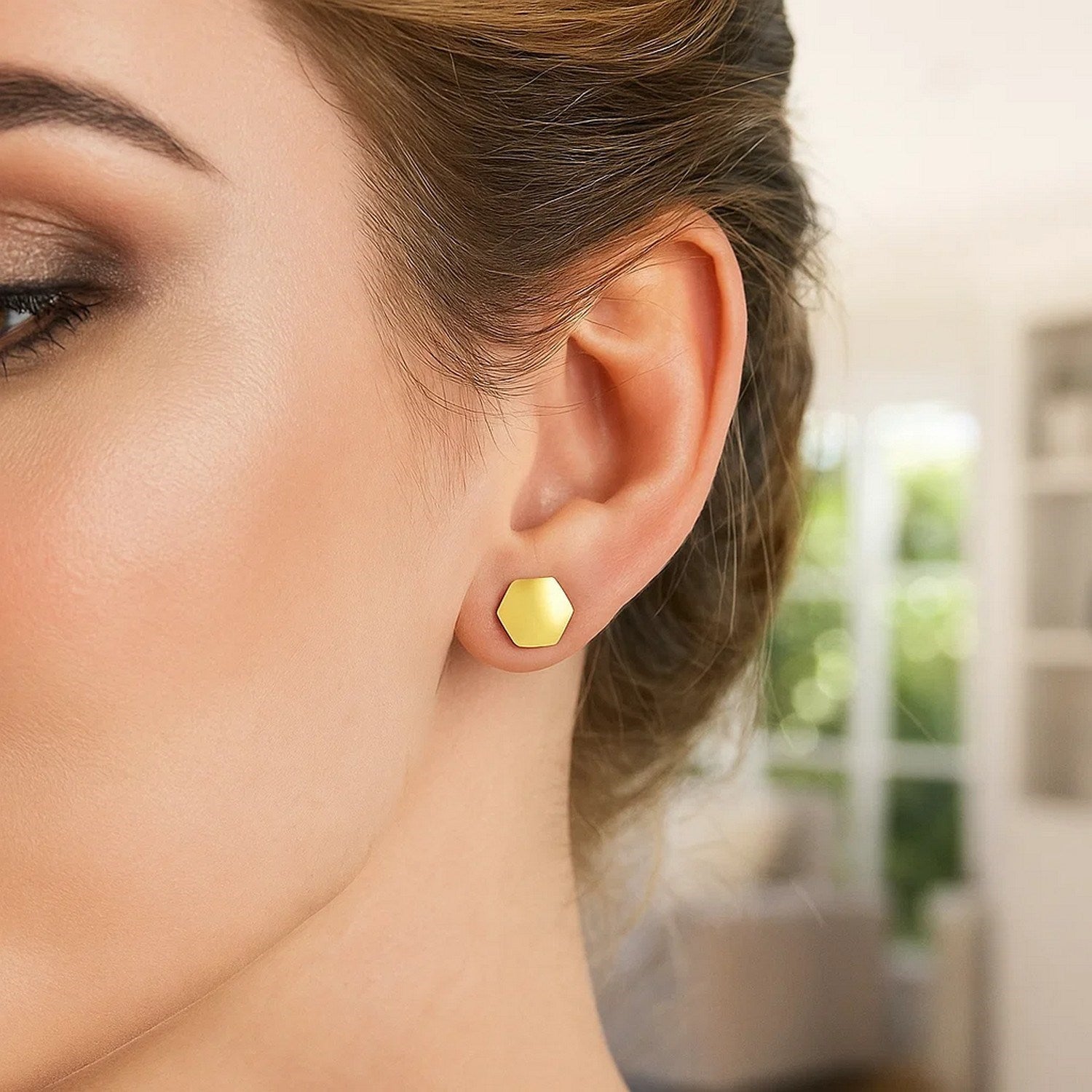 14k yellow gold hexagon stud earrings on a woman's ear.