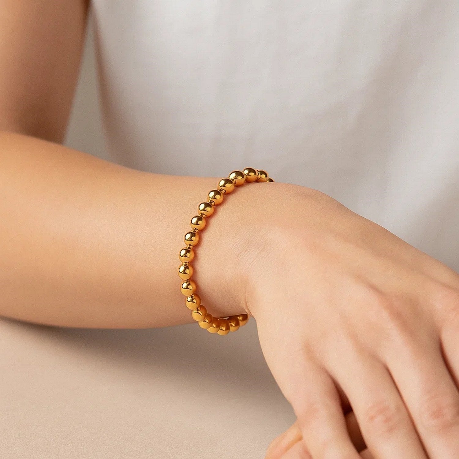 A polished 7mm bead bracelet in 14K yellow gold is worn on a wrist.