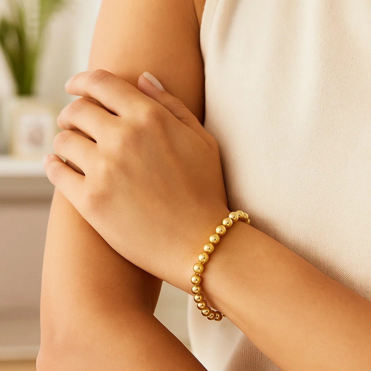 Polished 7mm bead bracelet in 14K yellow gold on a person's arm.