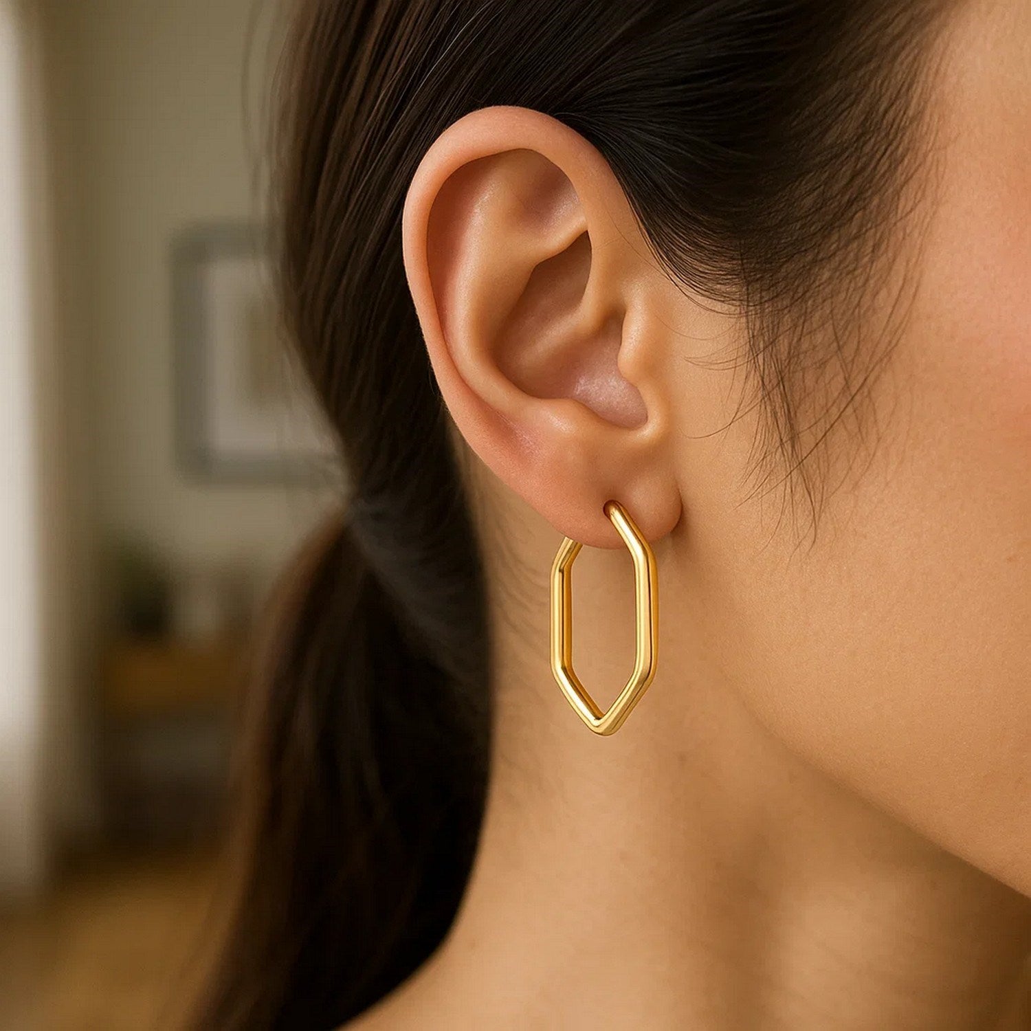 A woman wears a 14k yellow gold endless hexagon hoop earring.