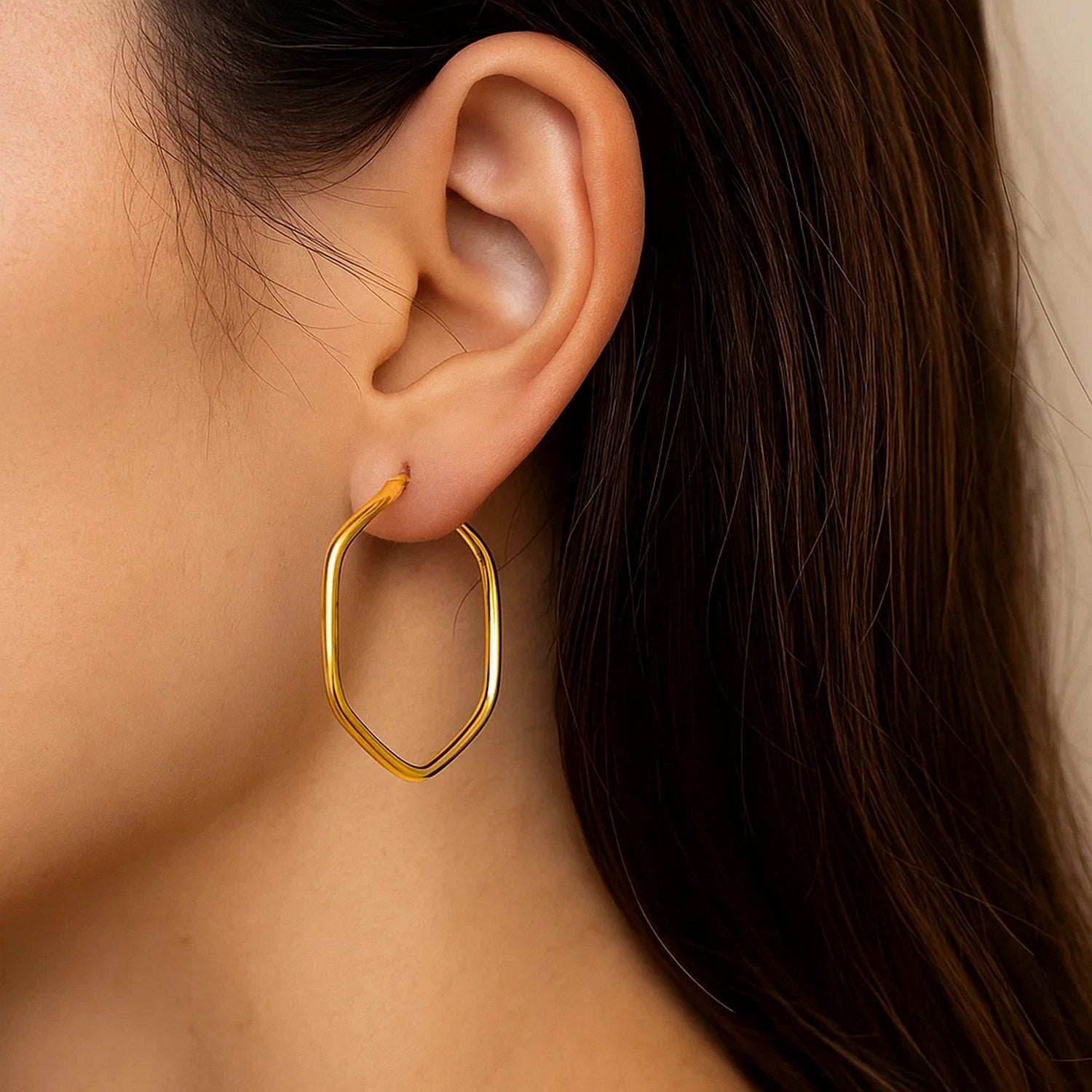 14K yellow gold hexagon hoop earrings with rounded edges on a person's ear.
