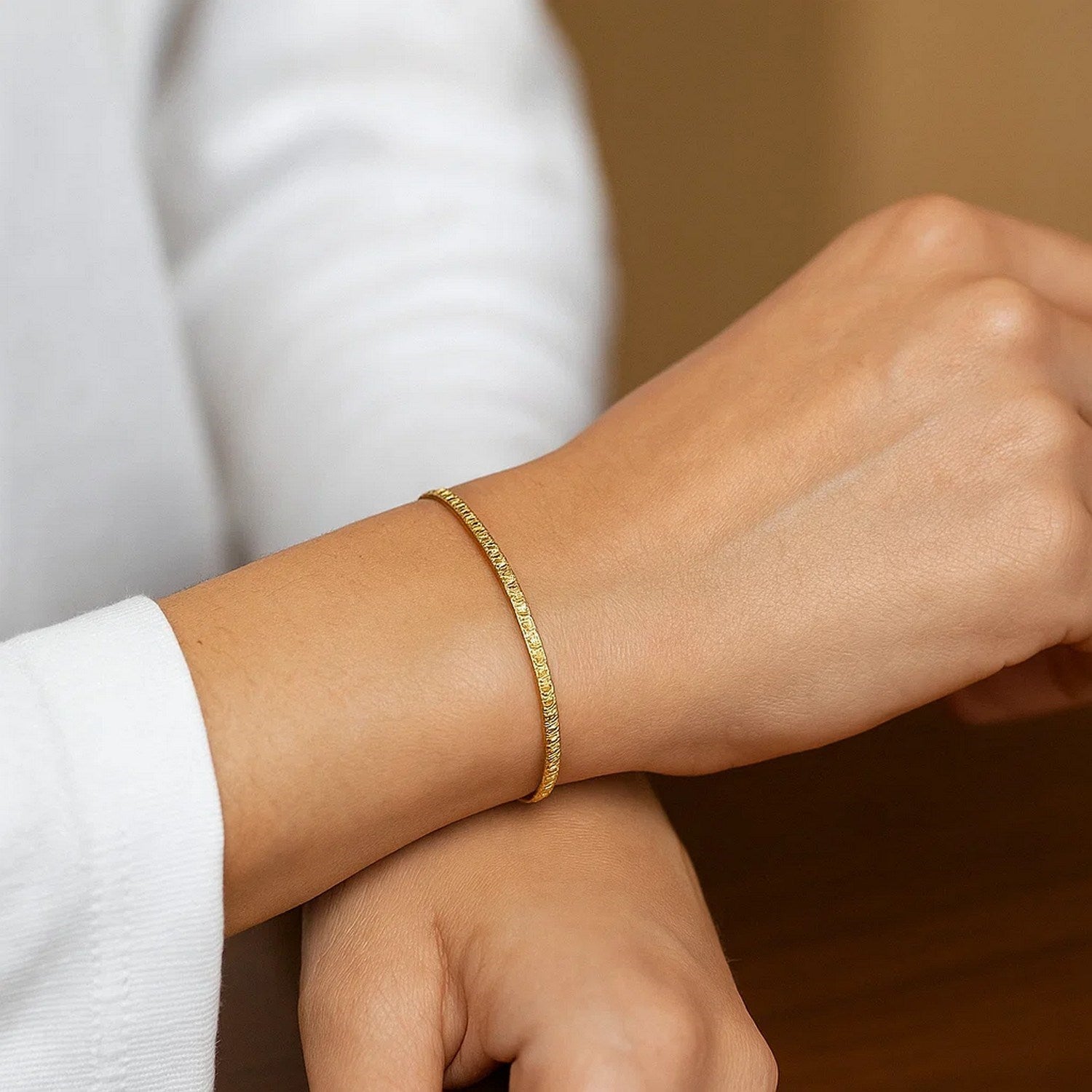 A woman wears a 14K yellow gold mini glacier bracelet on her left wrist.