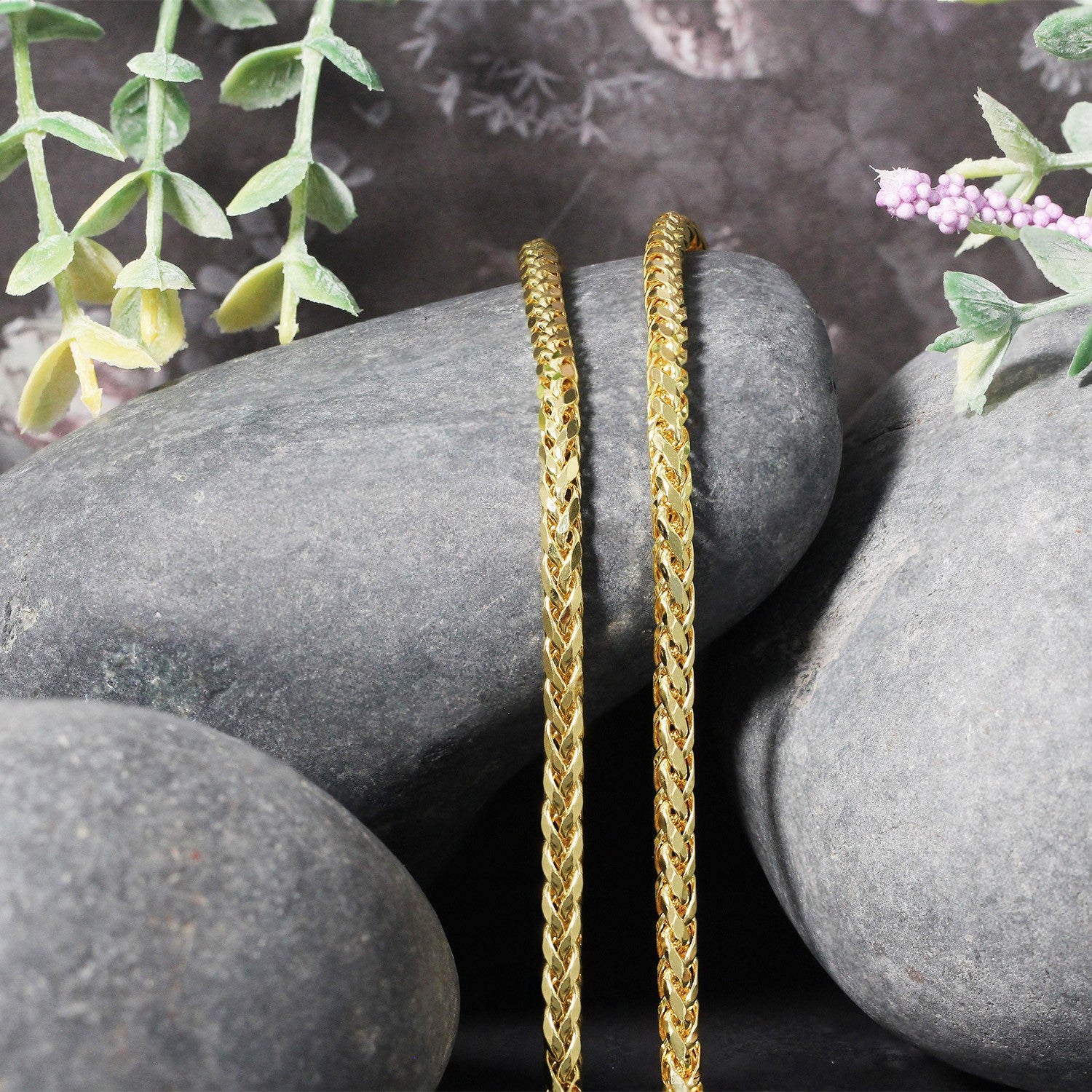A 14k yellow gold diamond-cut round Franco chain rests on grey stones.