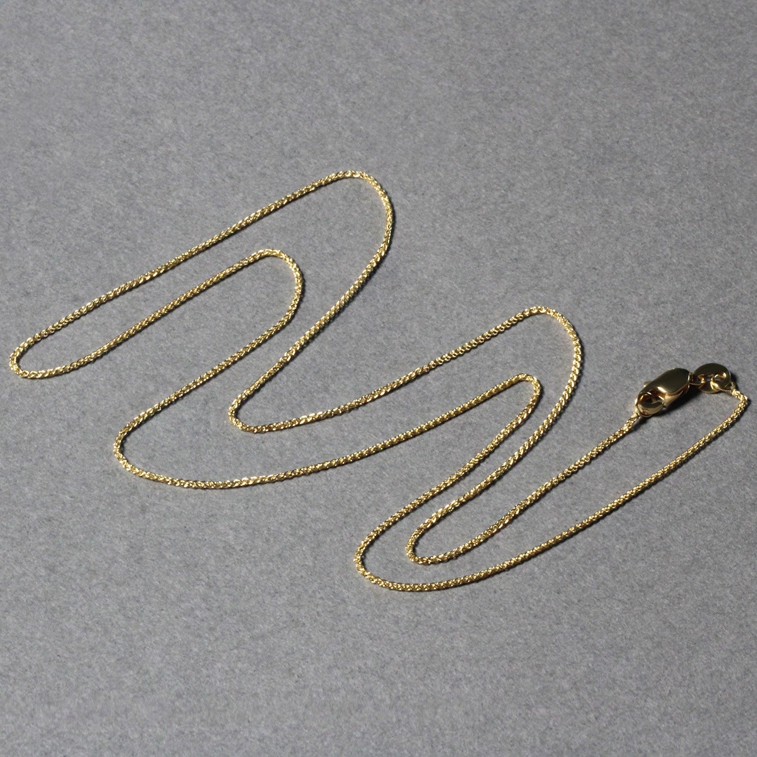 14k yellow gold round wheat chain with a lobster clasp on a gray background.