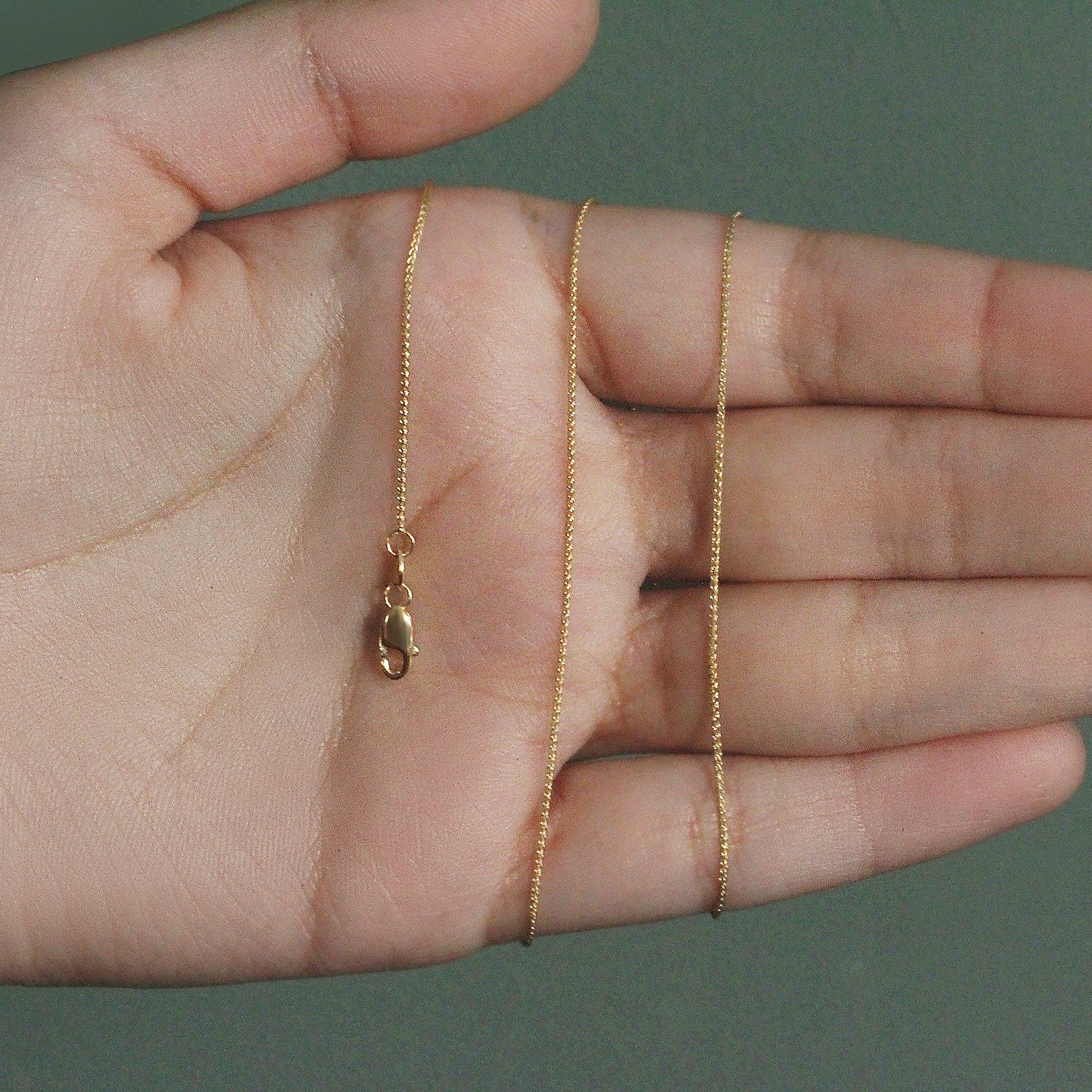 14k yellow gold round wheat chain with a lobster clasp held in a hand.