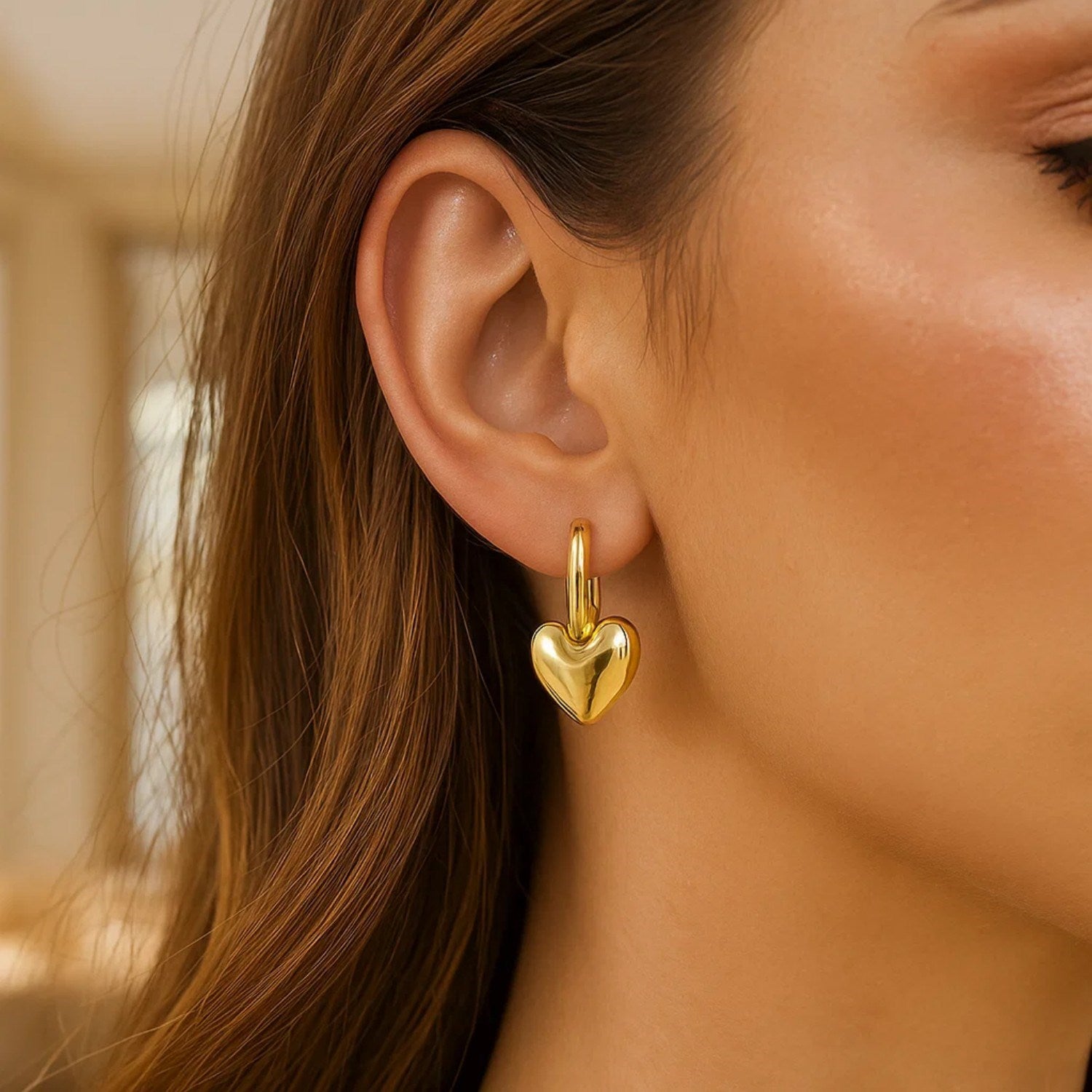 14K yellow gold puffy heart dangle huggie hoop earrings on a woman's ear.