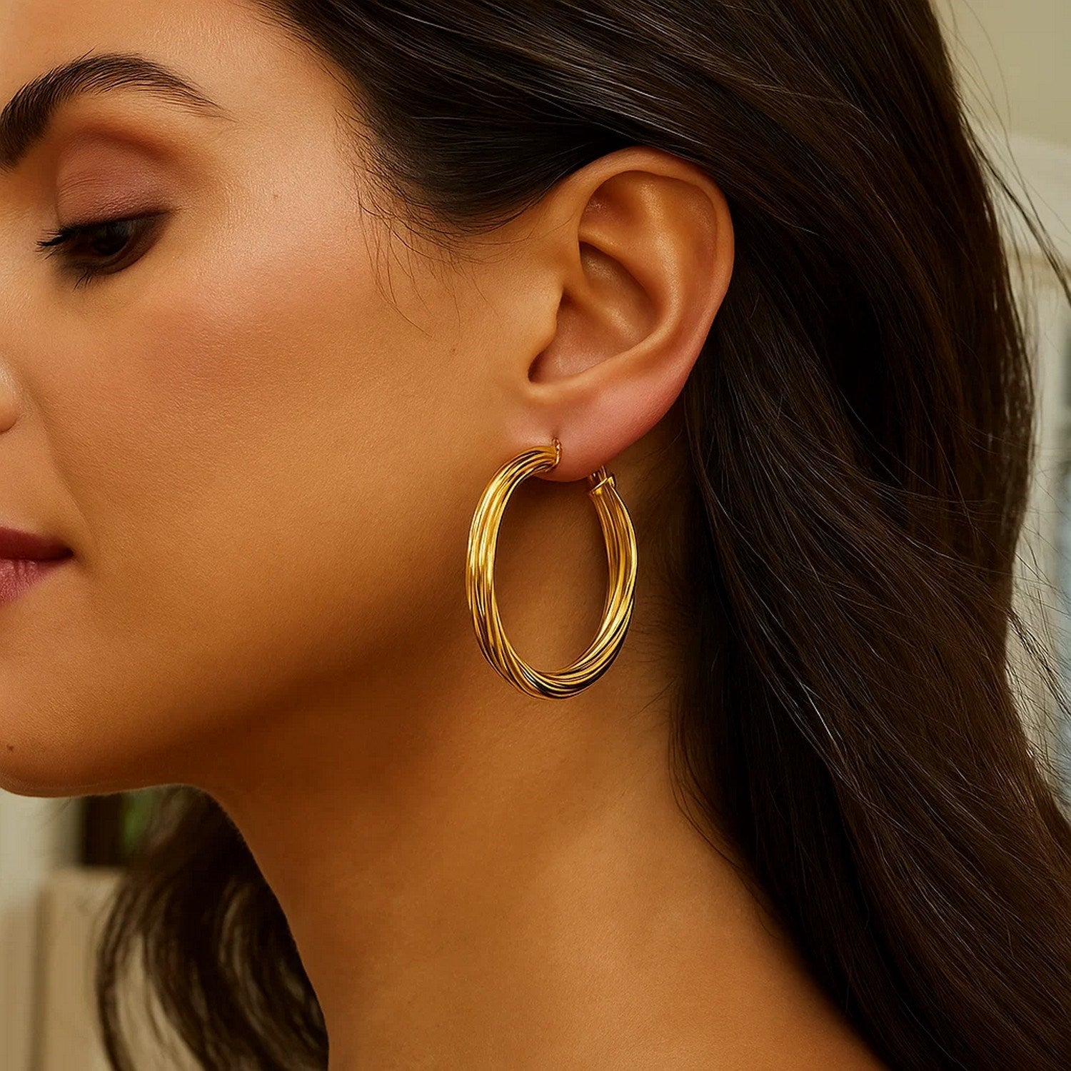 14K yellow gold full twist large hoop earrings on a woman's ear.
