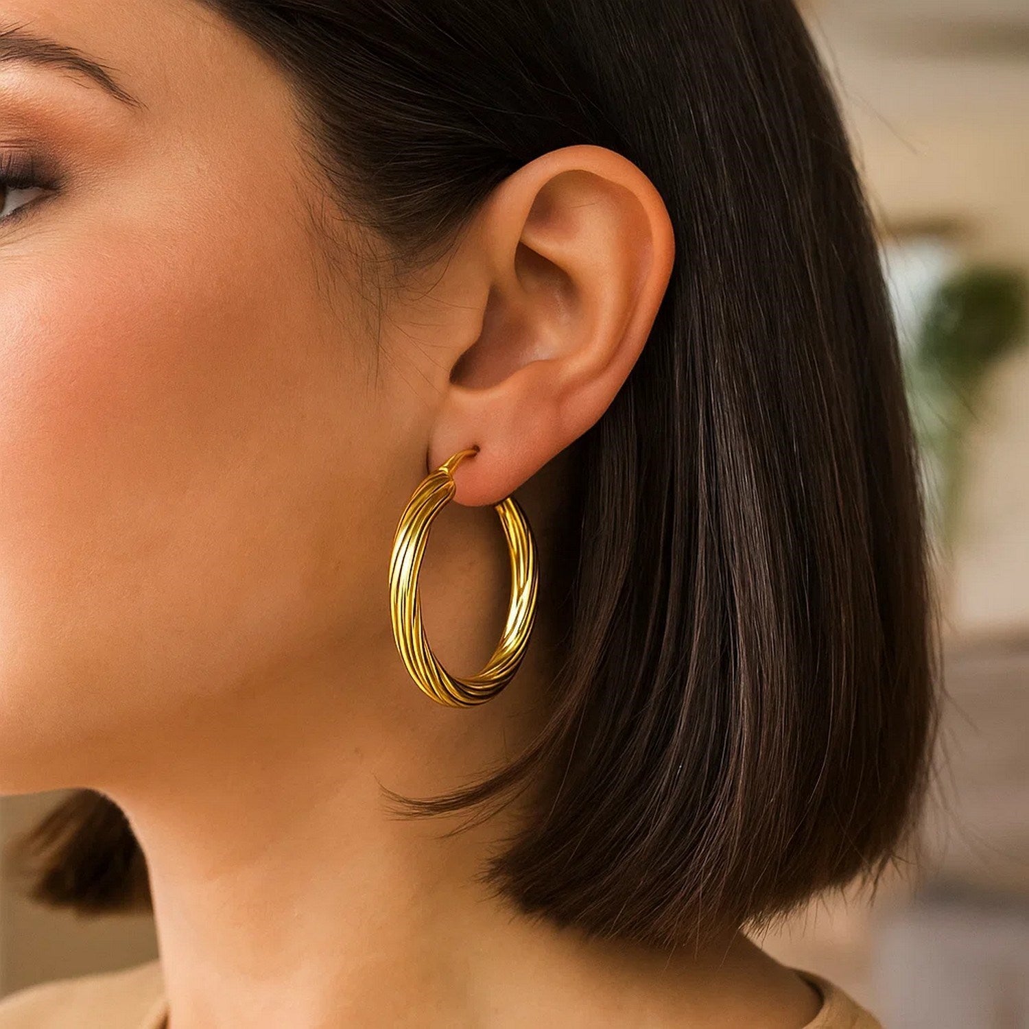 14K yellow gold full twist large hoop earrings on a woman's ear.