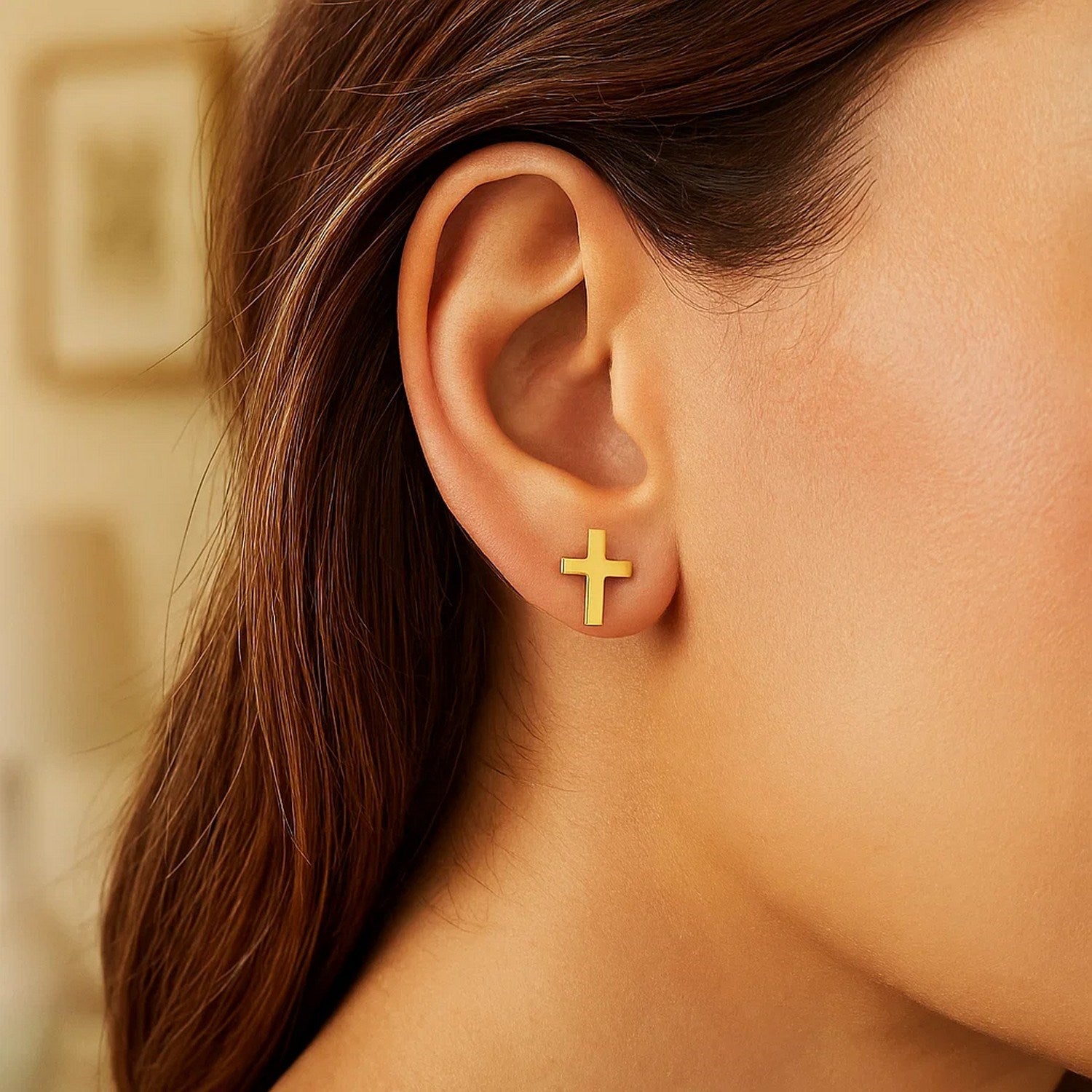 A woman wears a single 14k yellow gold cross post earring.