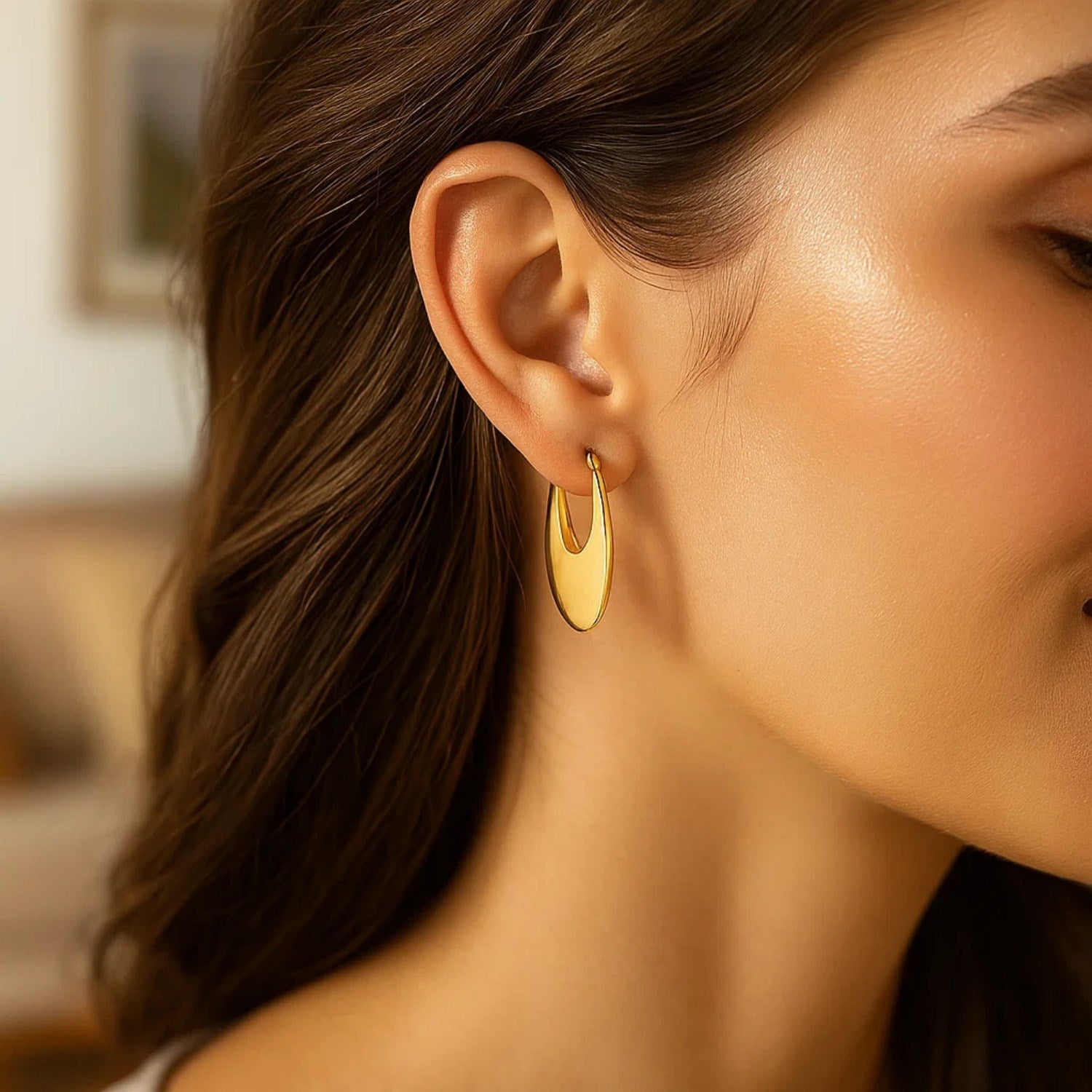 A woman wears a single polished 14K yellow gold oval hoop earring.