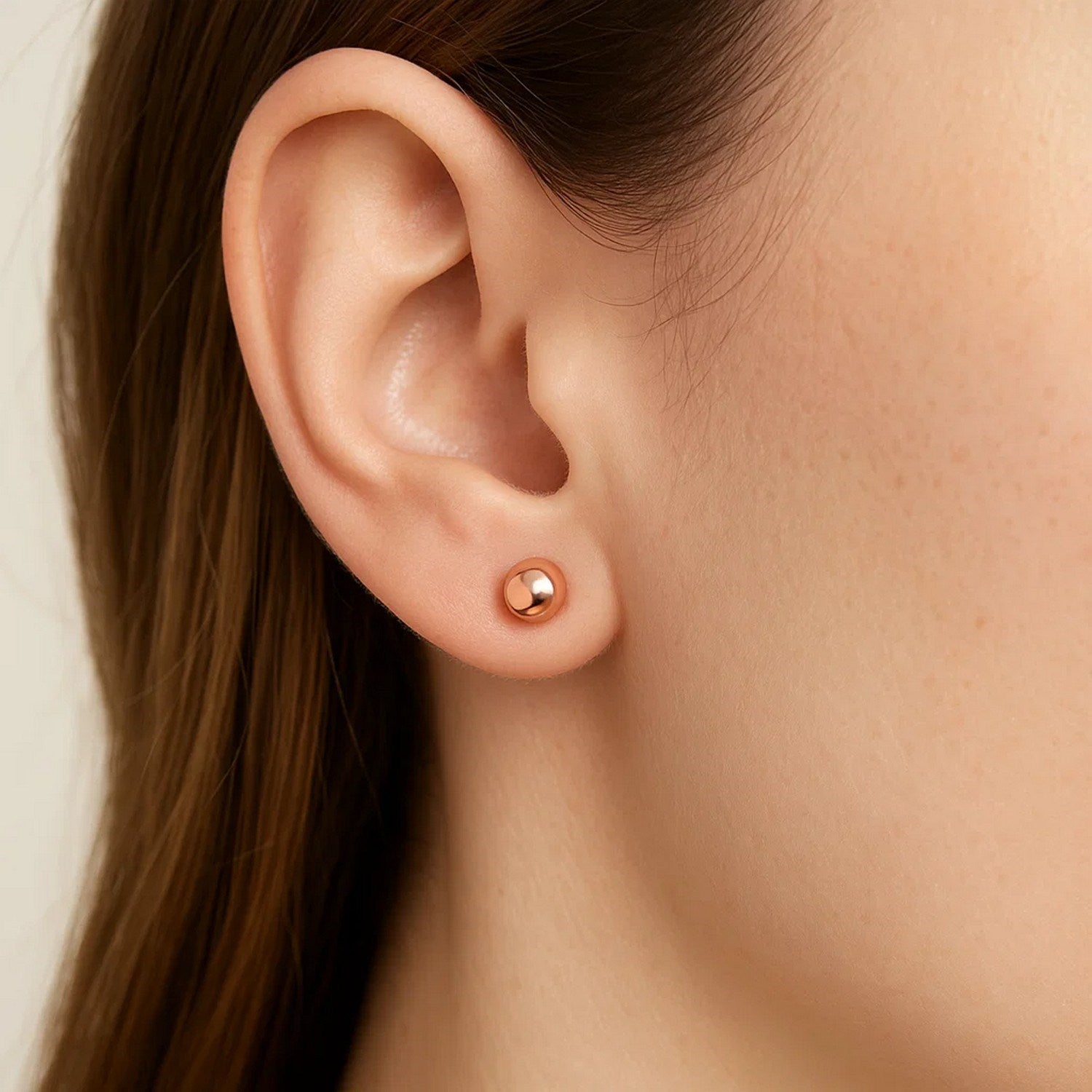 A woman wears a single 14k rose gold ball stud earring.