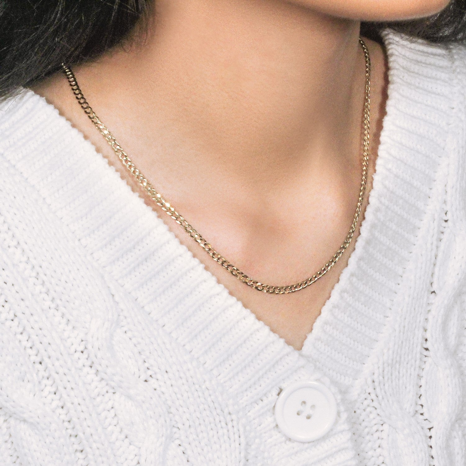A 14k yellow gold solid curb chain is worn around a person's neck over a white sweater.
