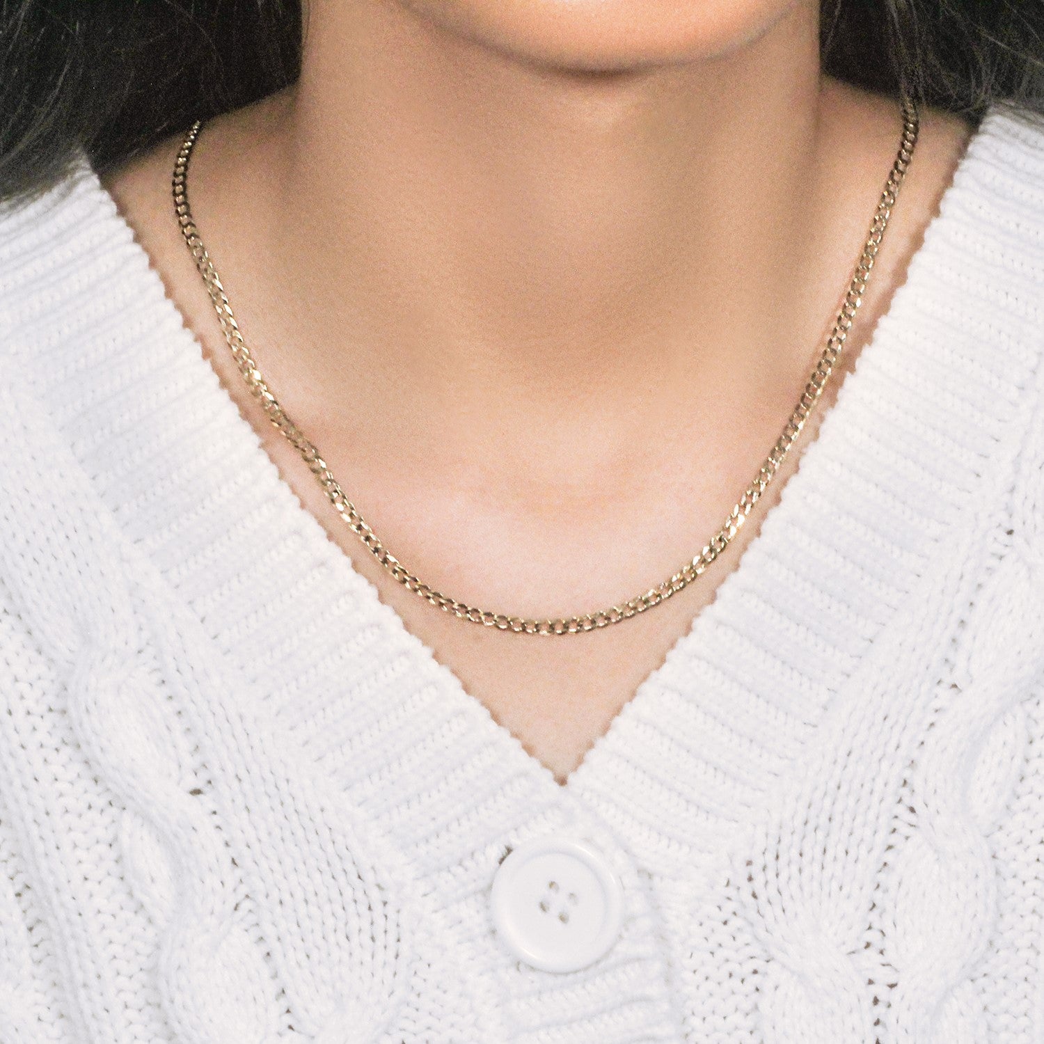 A 14k yellow gold solid curb chain is worn around a person's neck over a white sweater.