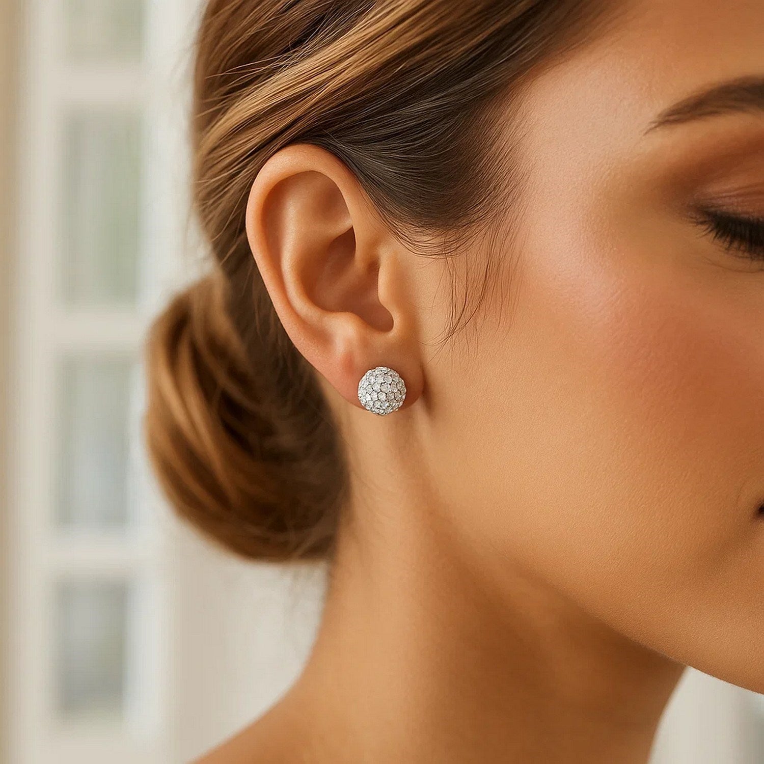 White tone crystal ball stud earring on a woman's ear.