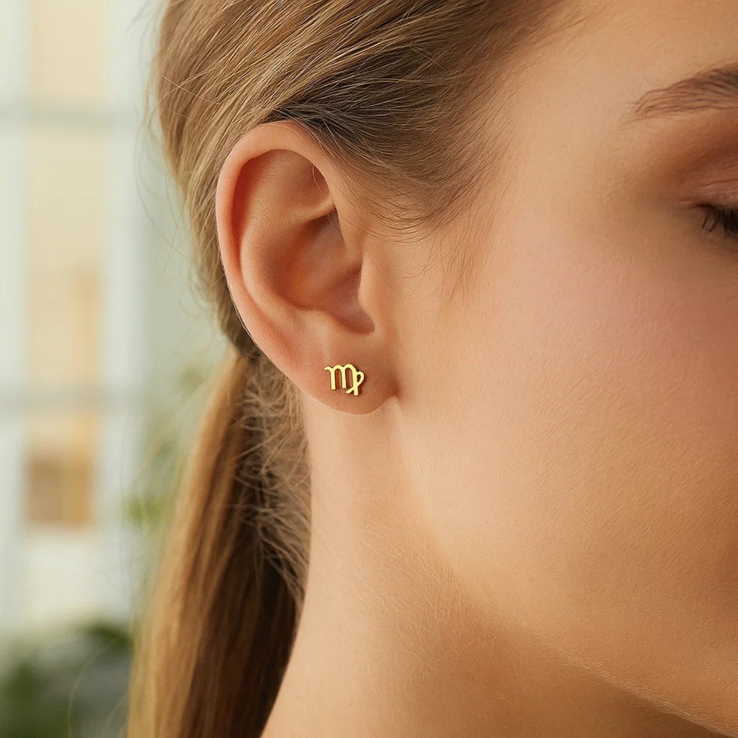 14k yellow gold Virgo stud earrings on a woman's ear.