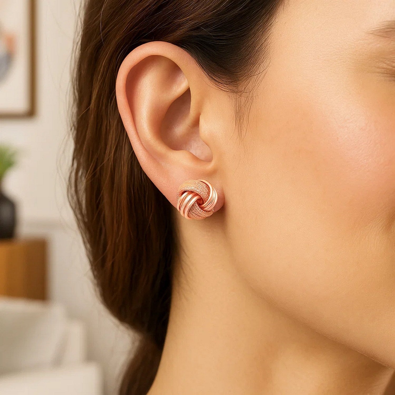 14k rose gold love knot earrings with ridge texture on a woman's ear.