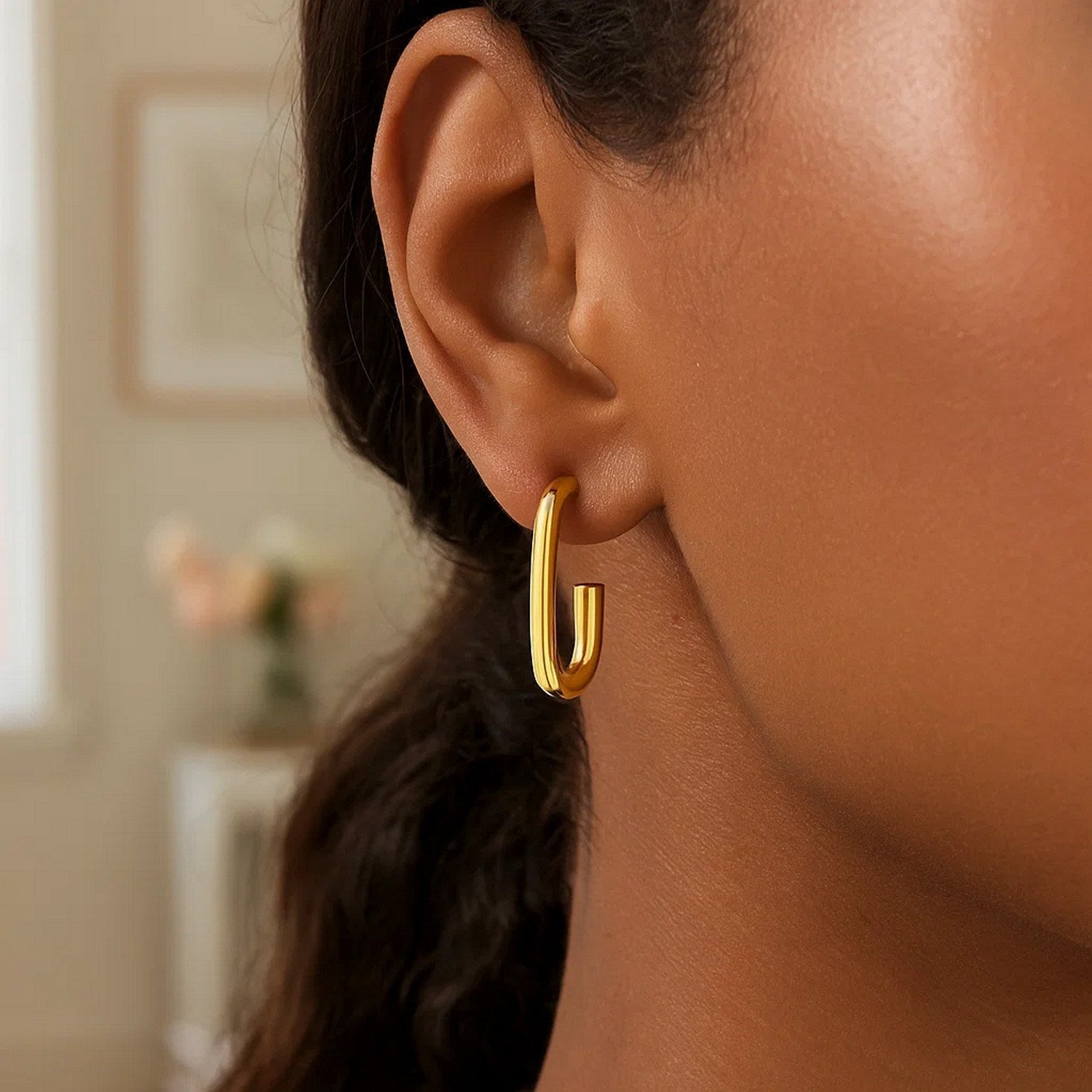 A woman wears a single polished 14K yellow gold paperclip hoop earring.