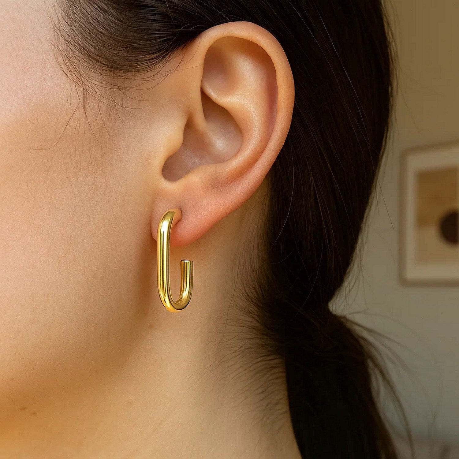 A woman wears a single 14K yellow gold paperclip hoop earring.