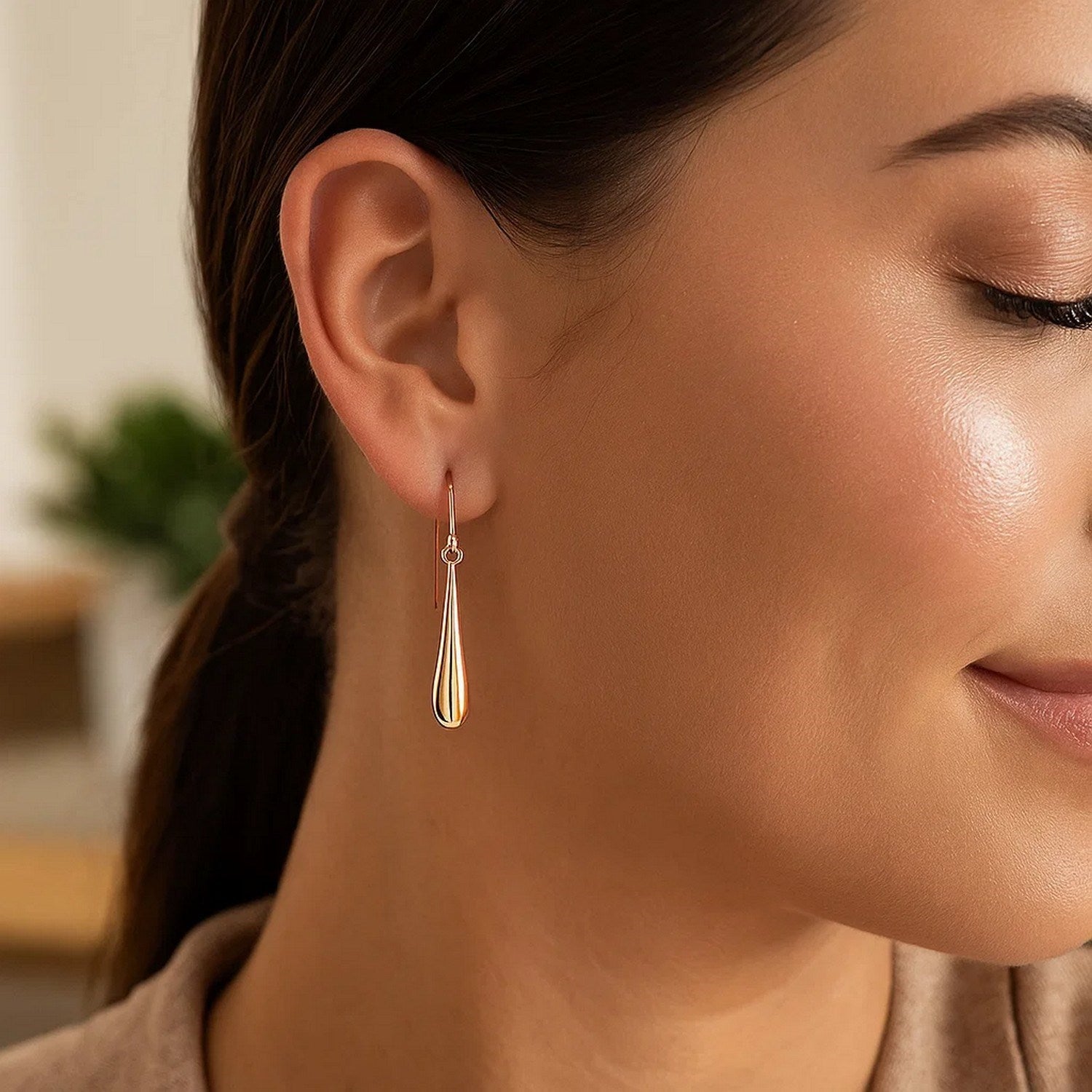 14k rose gold long polished teardrop dangling earrings on a woman's ear.