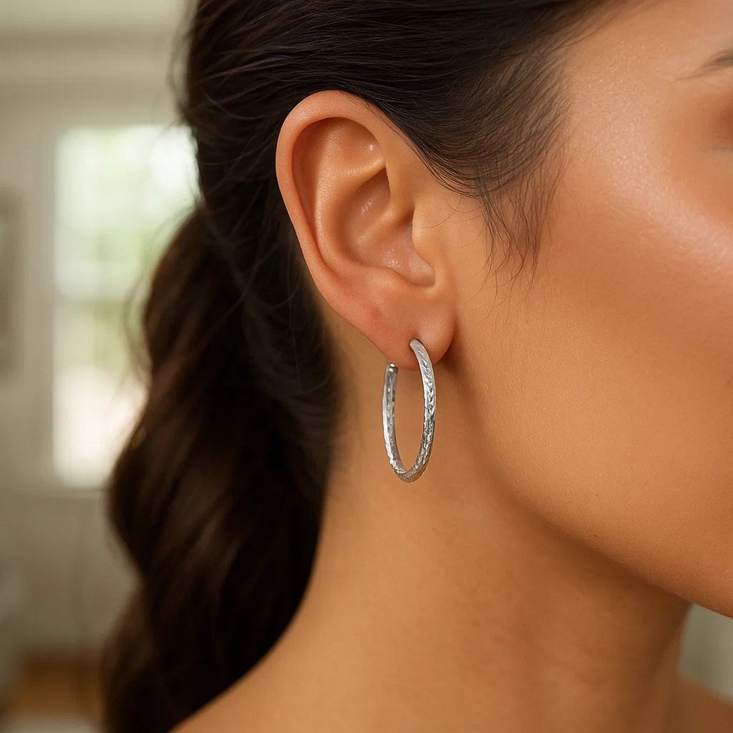 Sterling silver large hoop earrings with a hammered texture are worn on a woman's ear.