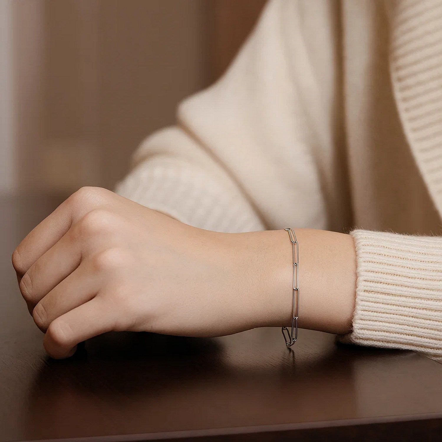 14k white gold paperclip bracelet on a person's wrist, wearing a cream sweater.