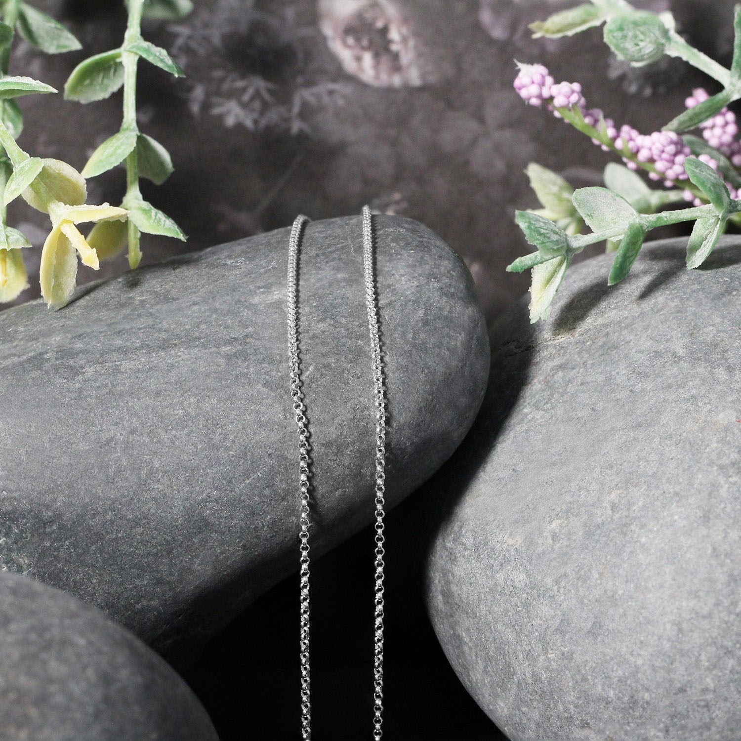14k white gold diamond cut rolo chain draped over smooth grey stones with foliage.