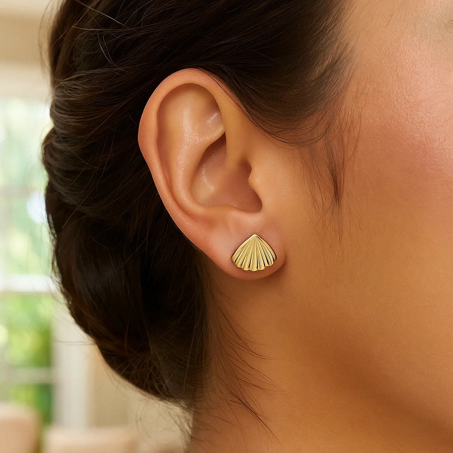 Sea shell stud earrings in 10K yellow gold on a woman's ear.