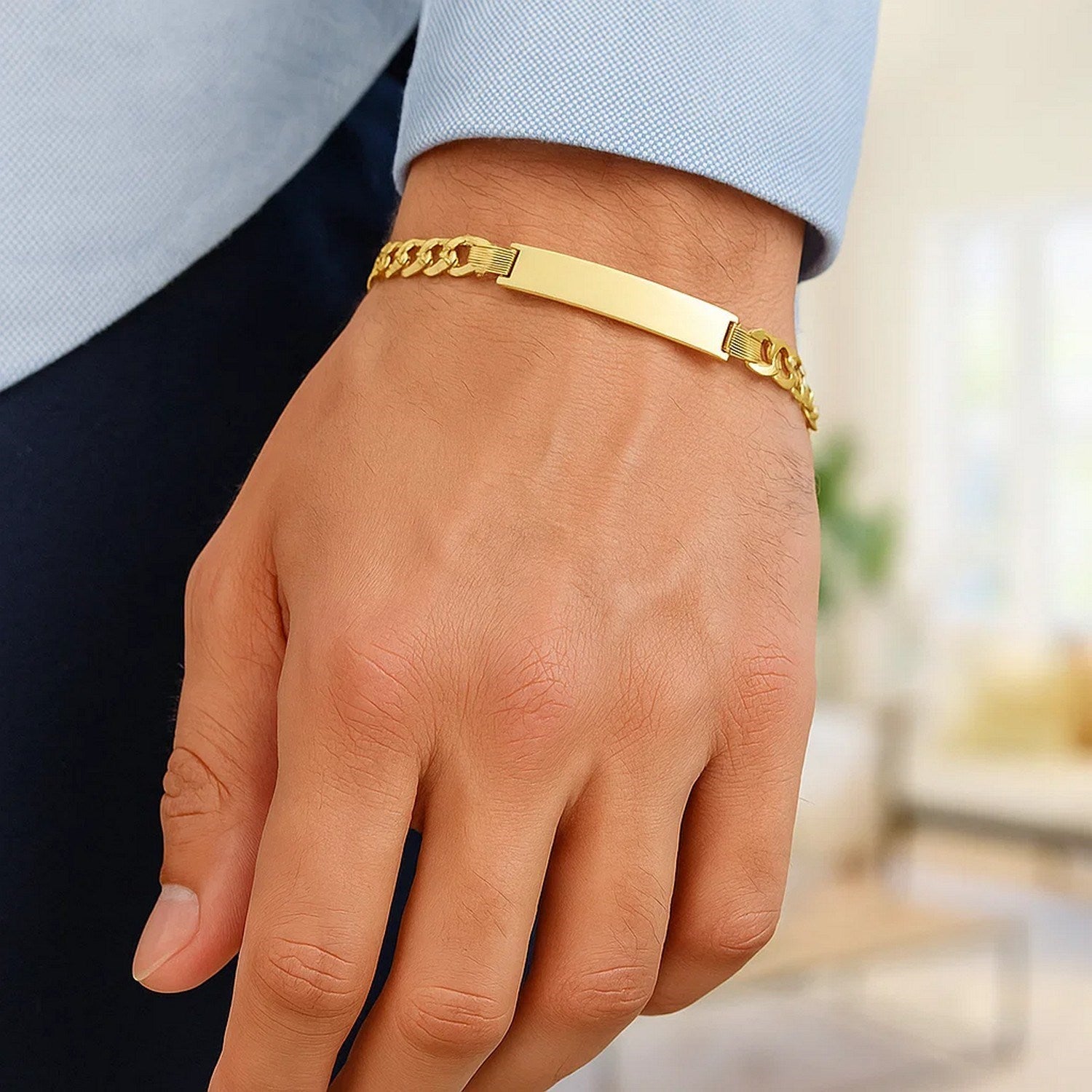 A man's wrist wears a polished 14k yellow gold curb chain ID bracelet.