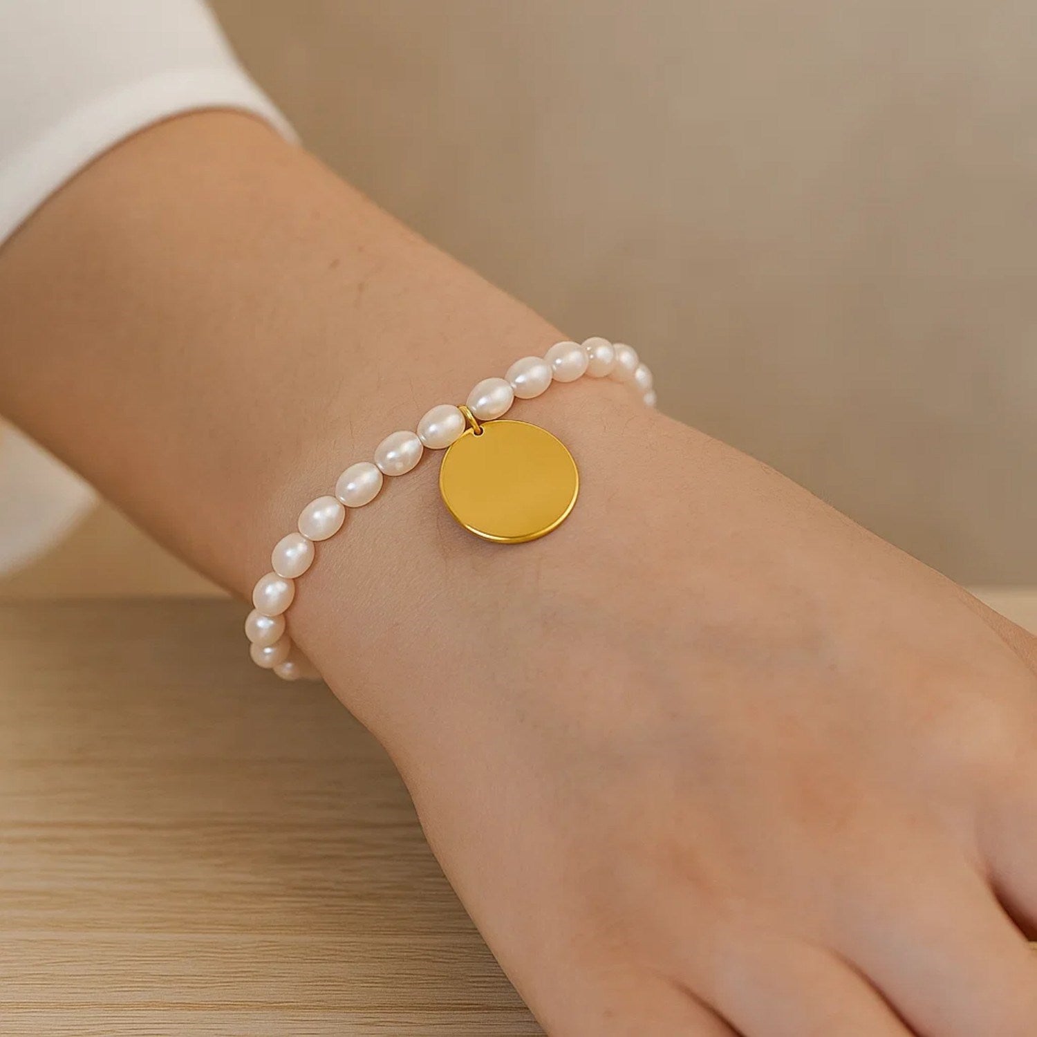 A 14k yellow gold pearl tag charm bracelet on a person's wrist.