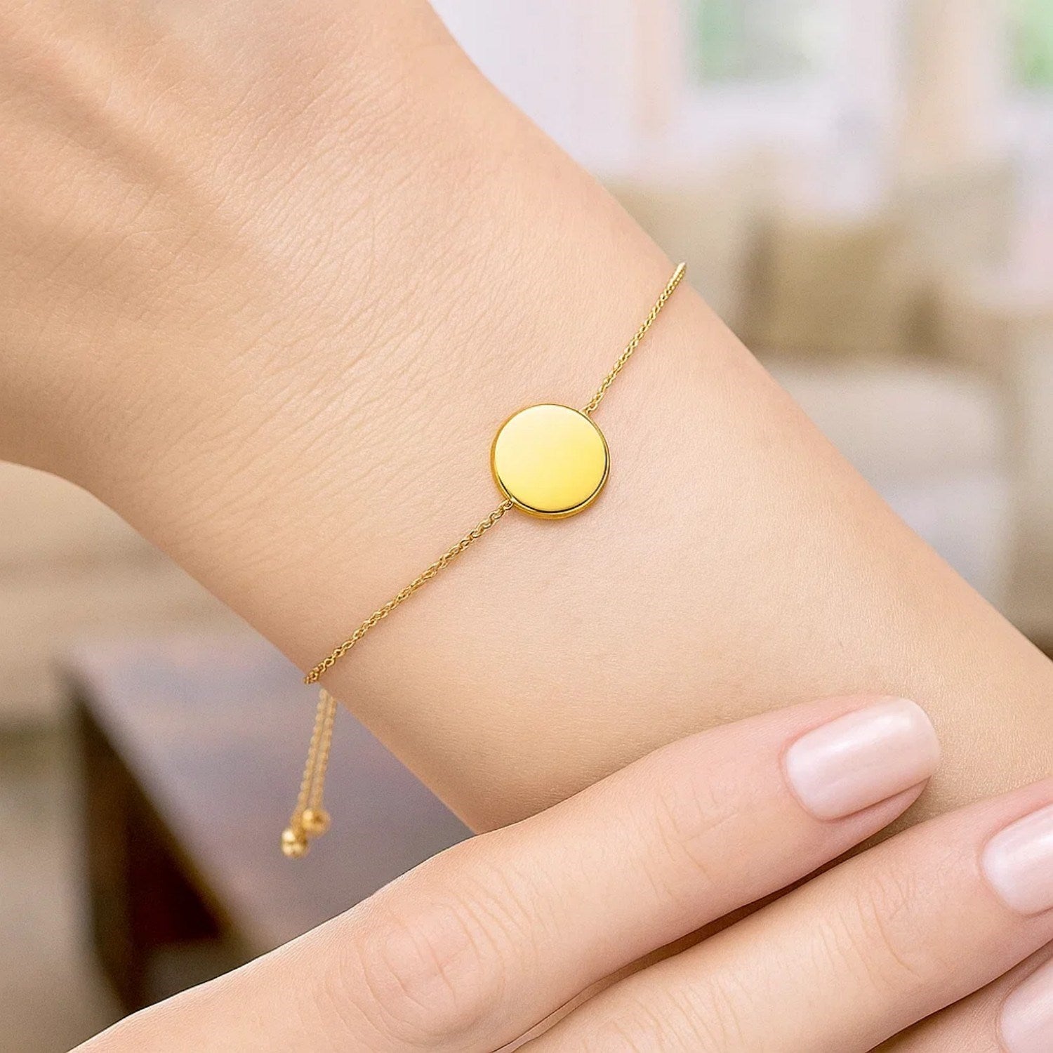 Adjustable 14k yellow gold bracelet with a shiny circular charm on a woman's wrist.
