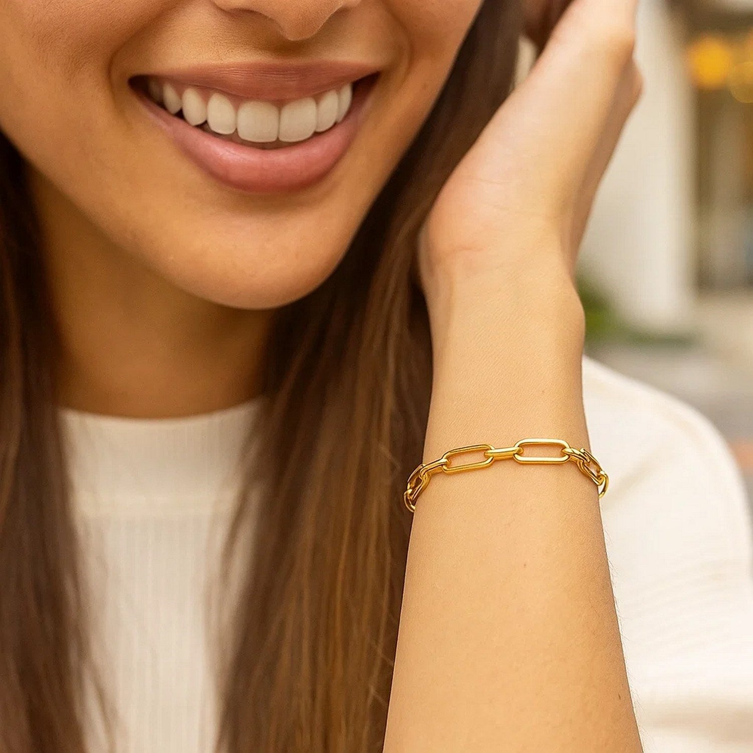 A woman smiles, wearing a 14k yellow gold paperclip chain bracelet on her left wrist.