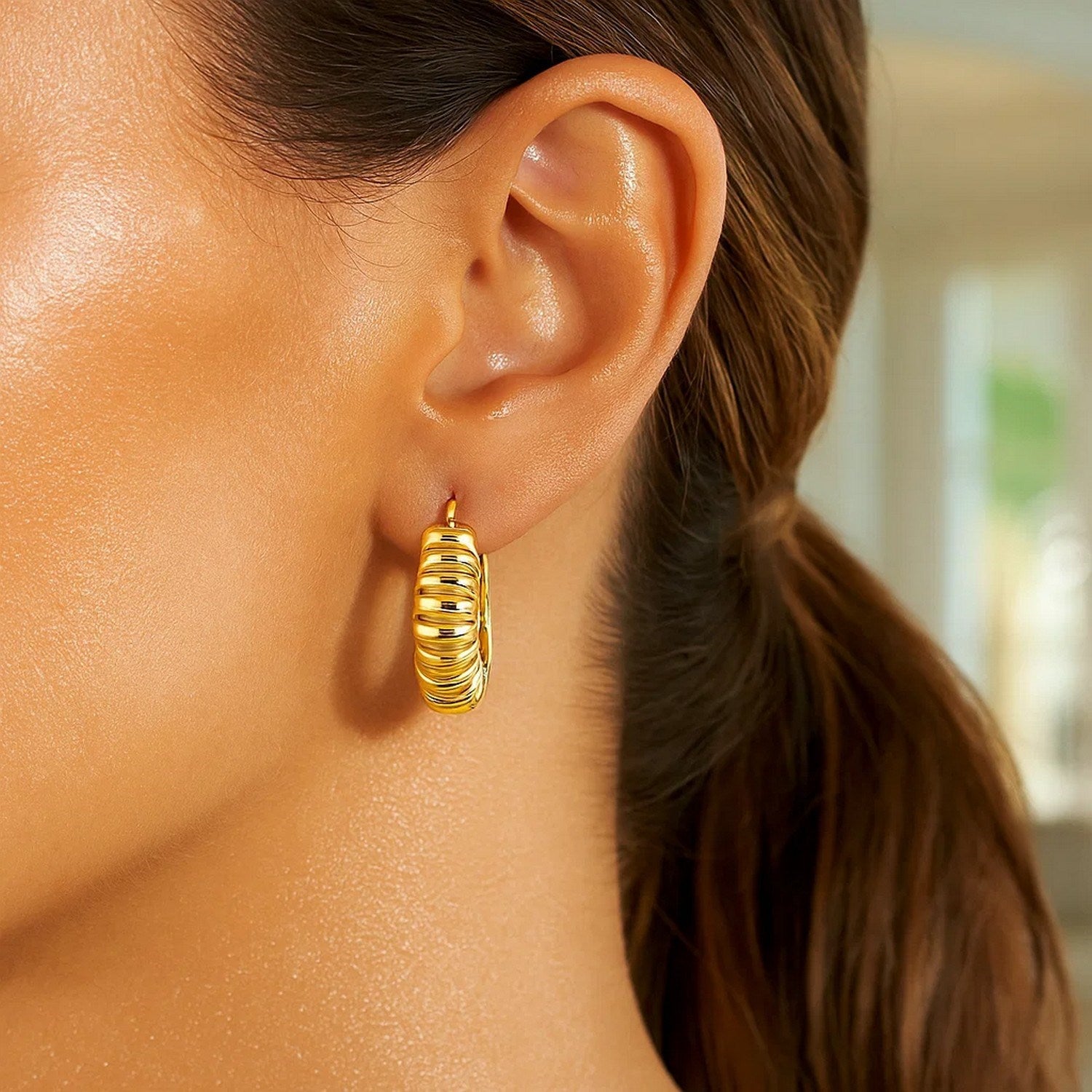 14K yellow gold polished puffed ribbed hoop earrings on a woman's ear.