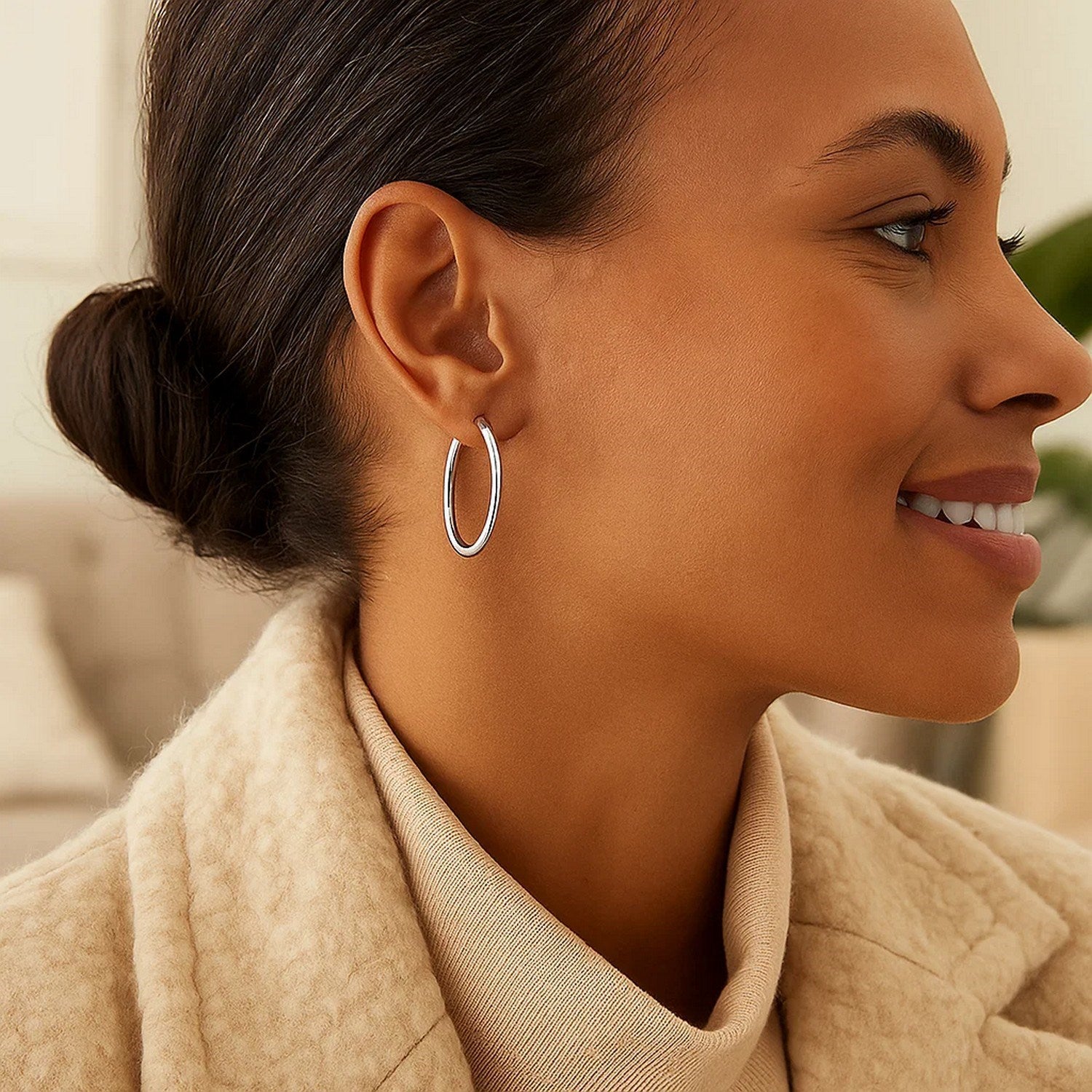 A woman wears a single polished white gold hoop earring.